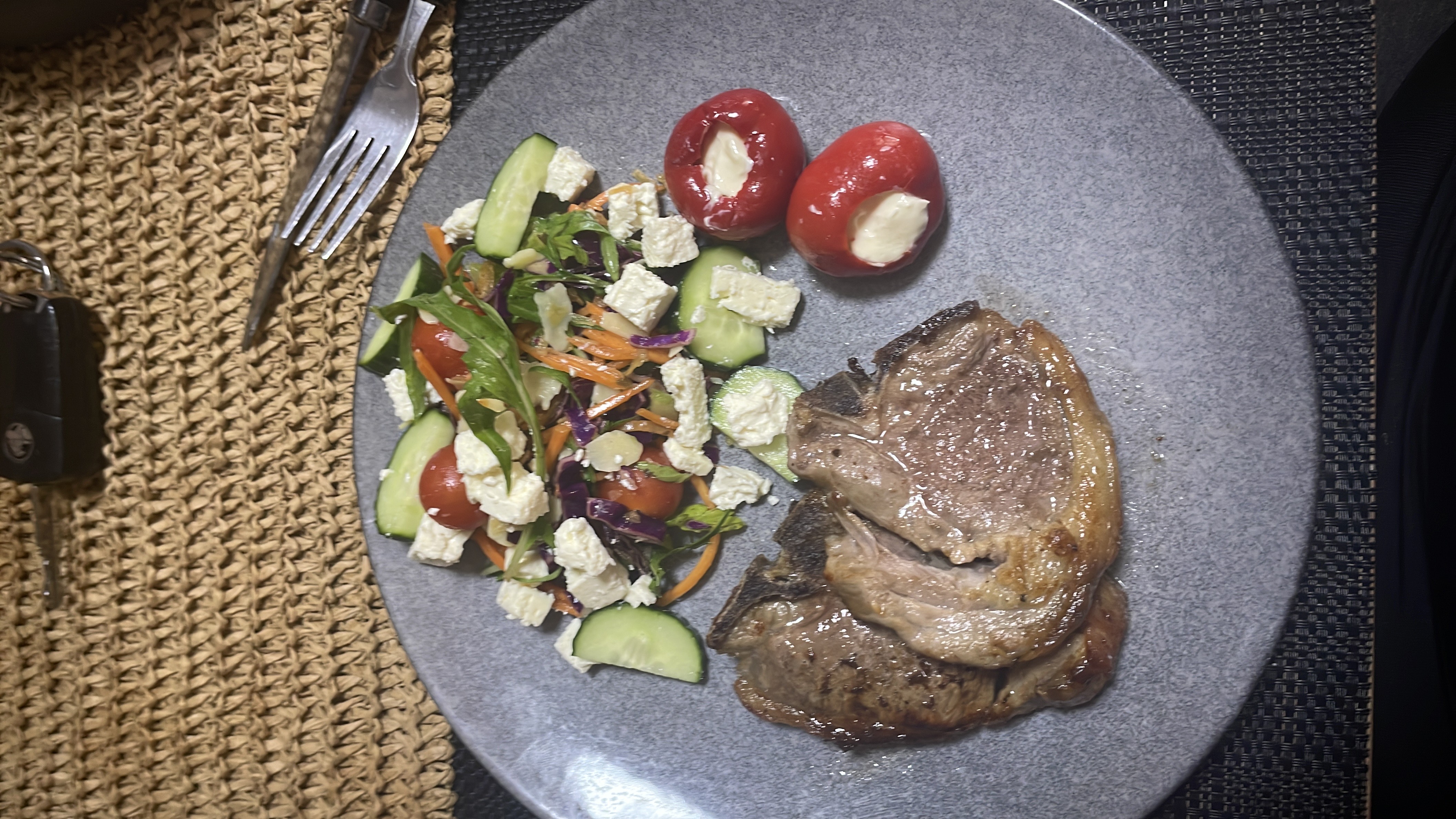 A balanced meal consisting of lamb chops, a mixed salad with vegetables and feta cheese, and stuffed cherry peppers.