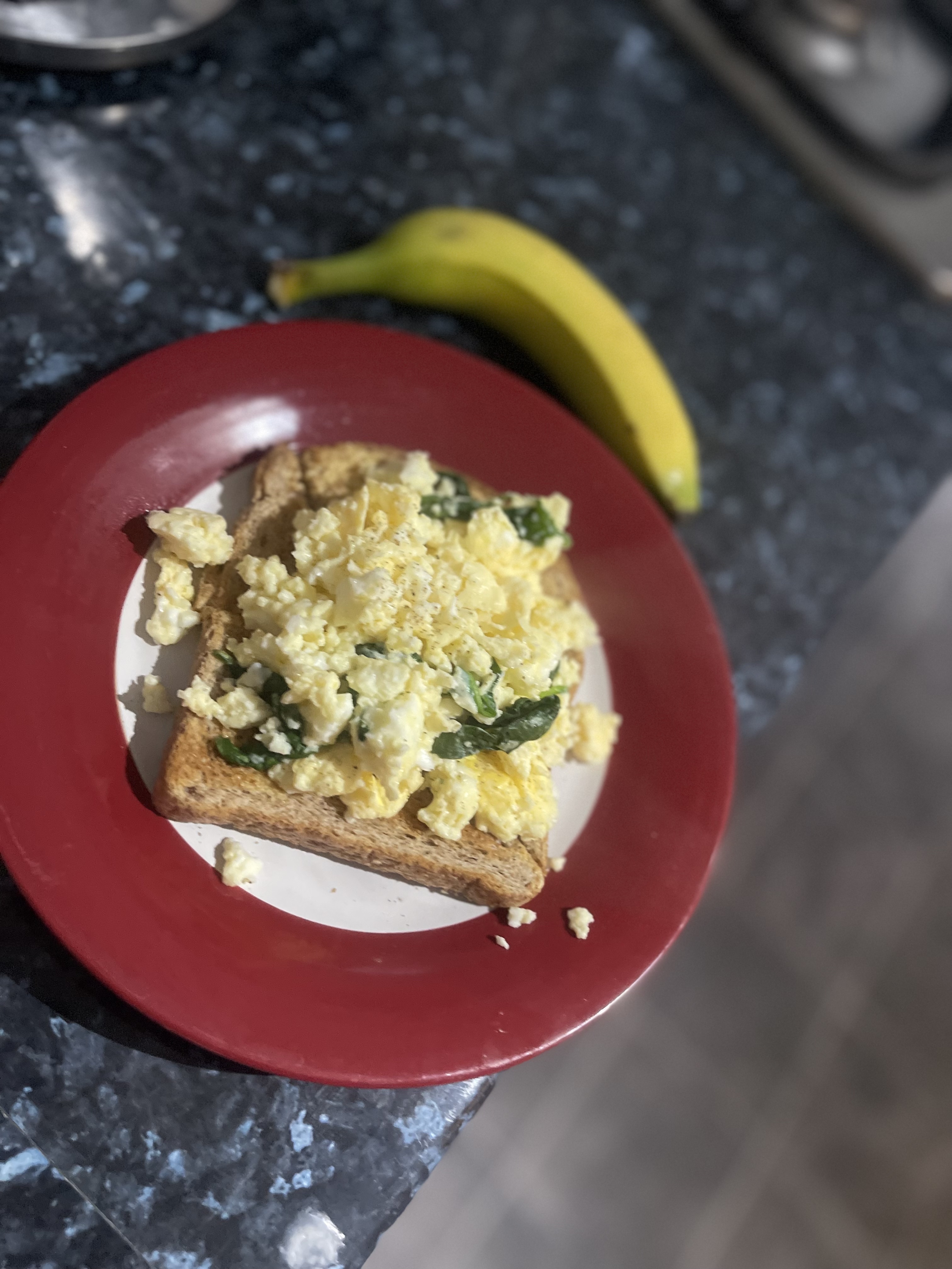 A nutritious breakfast consisting of whole grain toast topped with scrambled eggs and spinach, served with a banana.