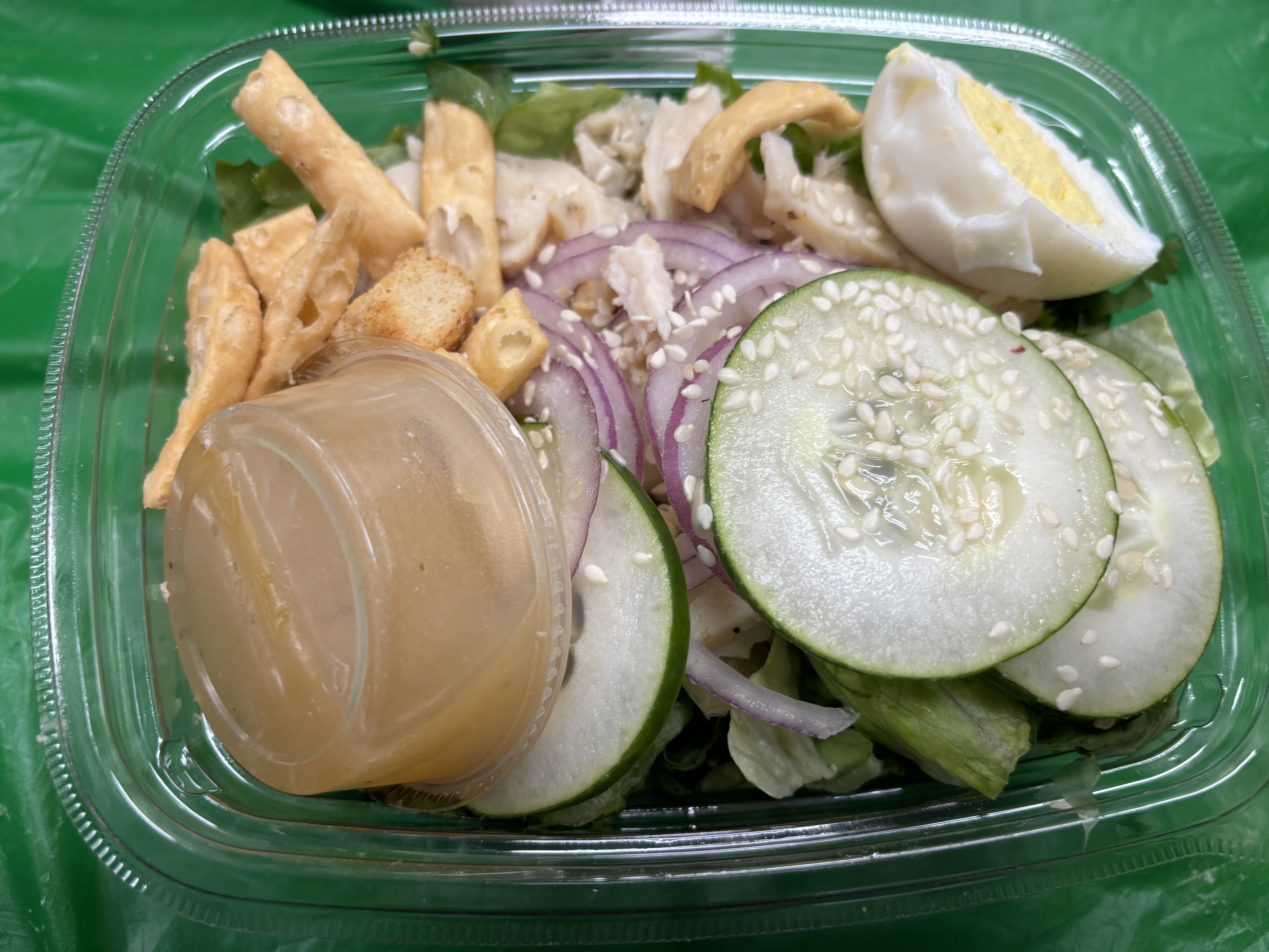 A fresh salad containing lettuce, cucumber, red onion, boiled egg, sesame seeds, croutons, and dressing.