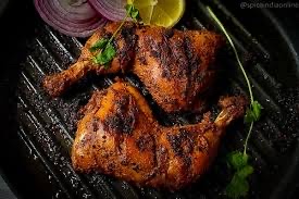 Grilled chicken legs seasoned with spices, garnished with onion, lemon, and cilantro.