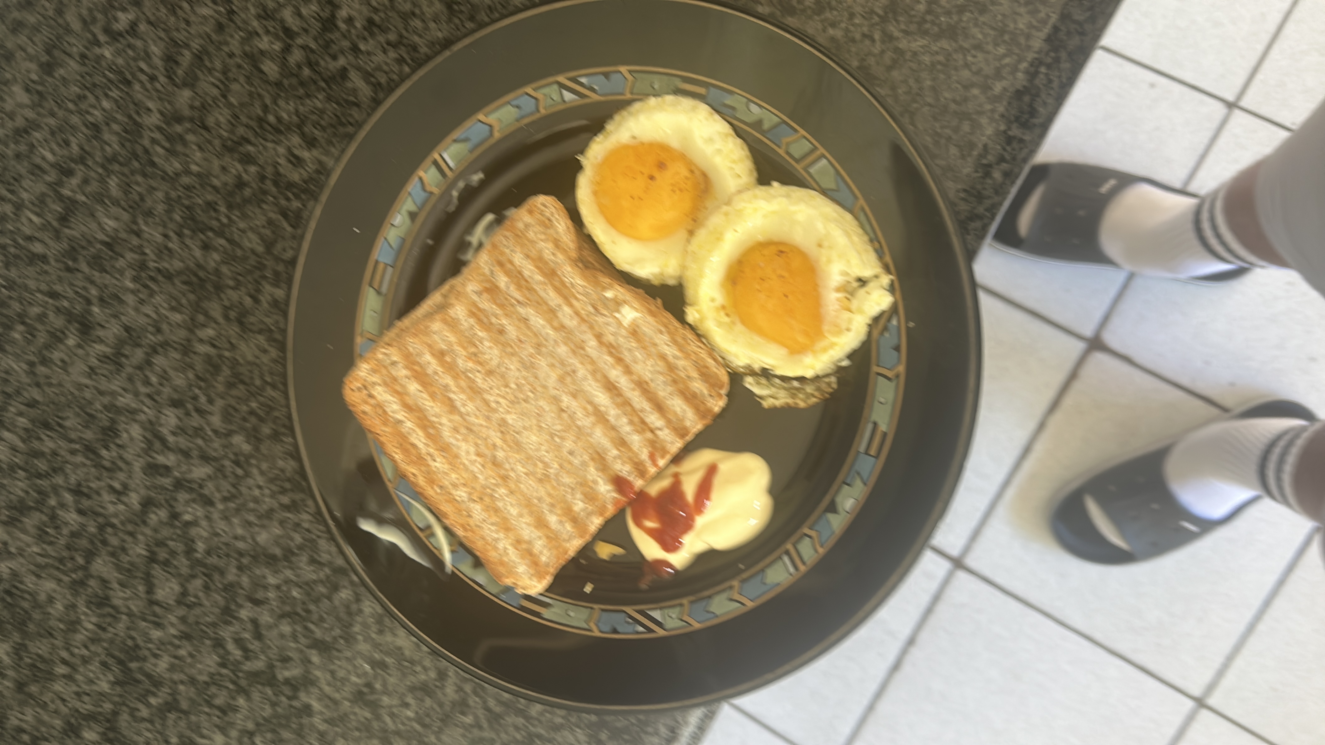 A plate containing two fried eggs, a slice of toasted bread, and condiments including mayonnaise and ketchup.