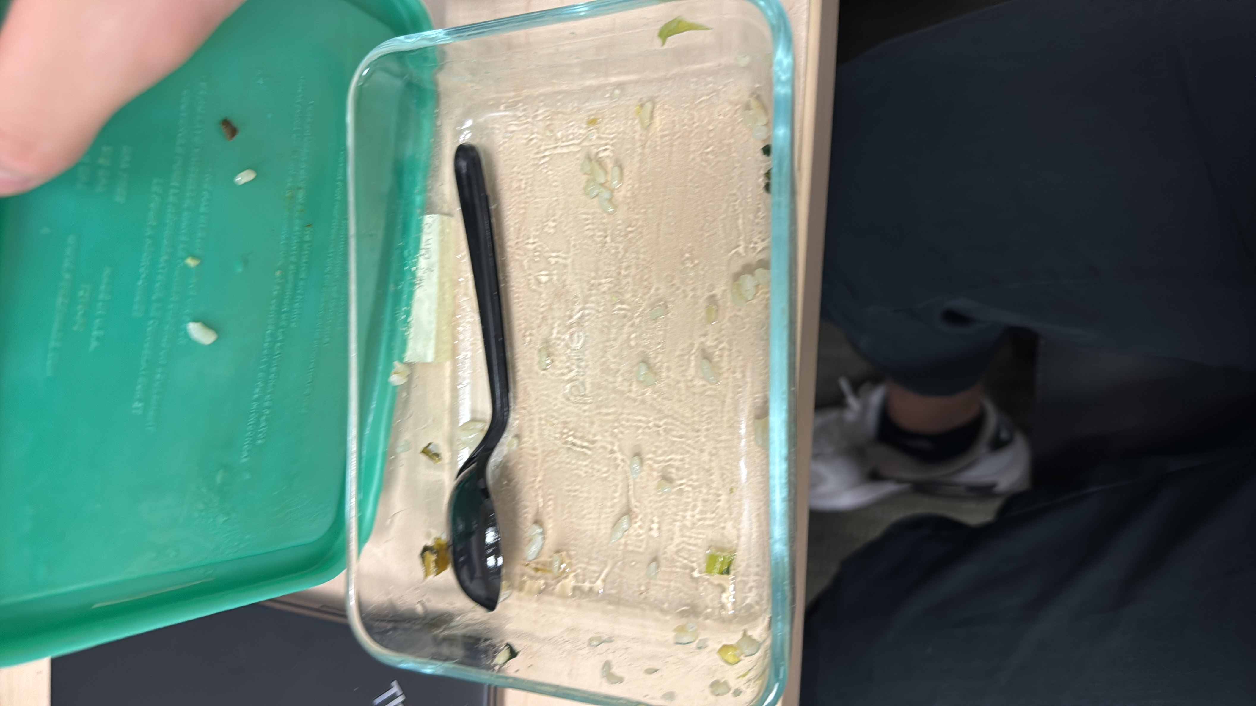 The image shows an empty food container with minimal leftover food, including small pieces of rice and vegetables.