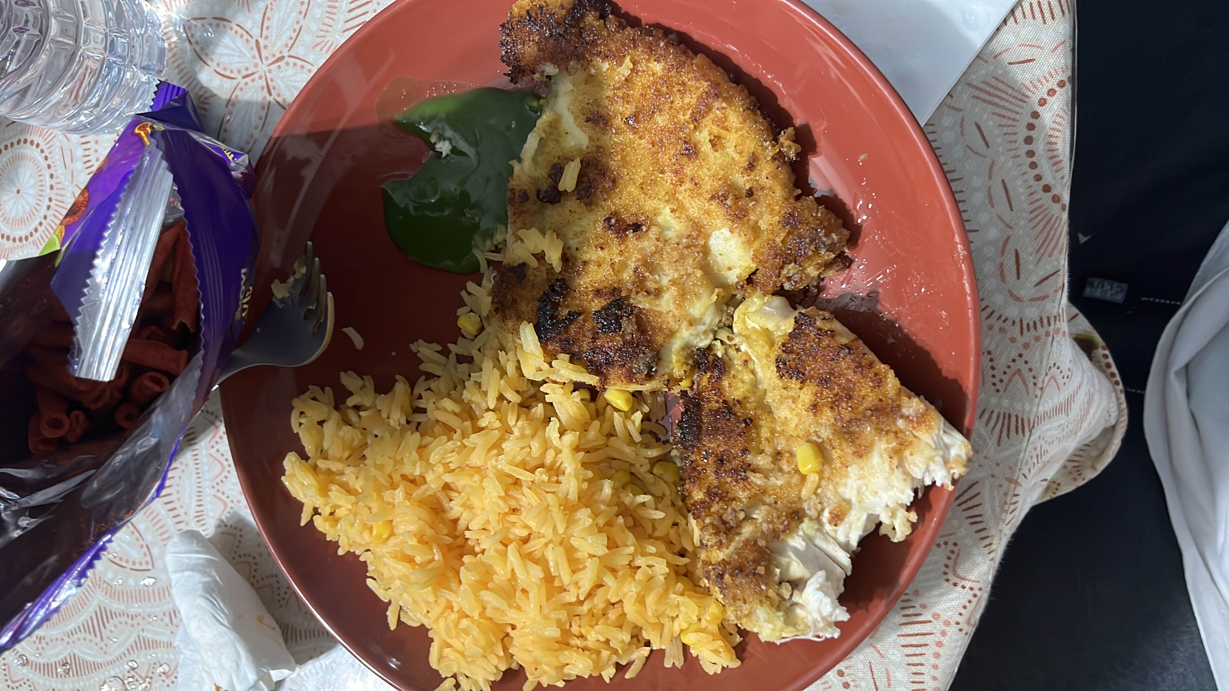 A meal consisting of breaded chicken, yellow rice, green sauce, and a side of snack chips.