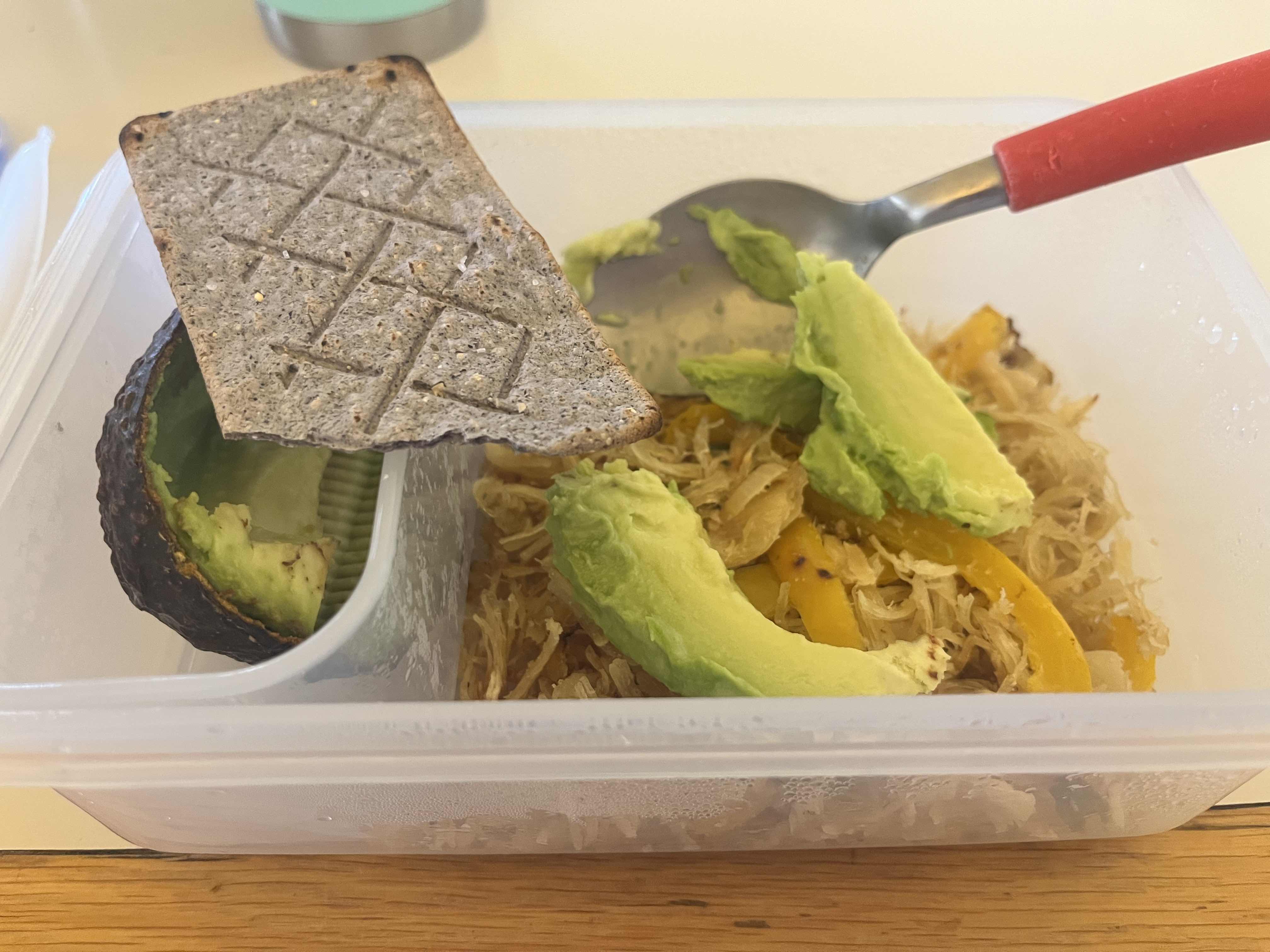 A healthy meal consisting of avocado, shredded chicken, yellow bell pepper, and crispbread, providing a balanced mix of protein, fats, and carbs.