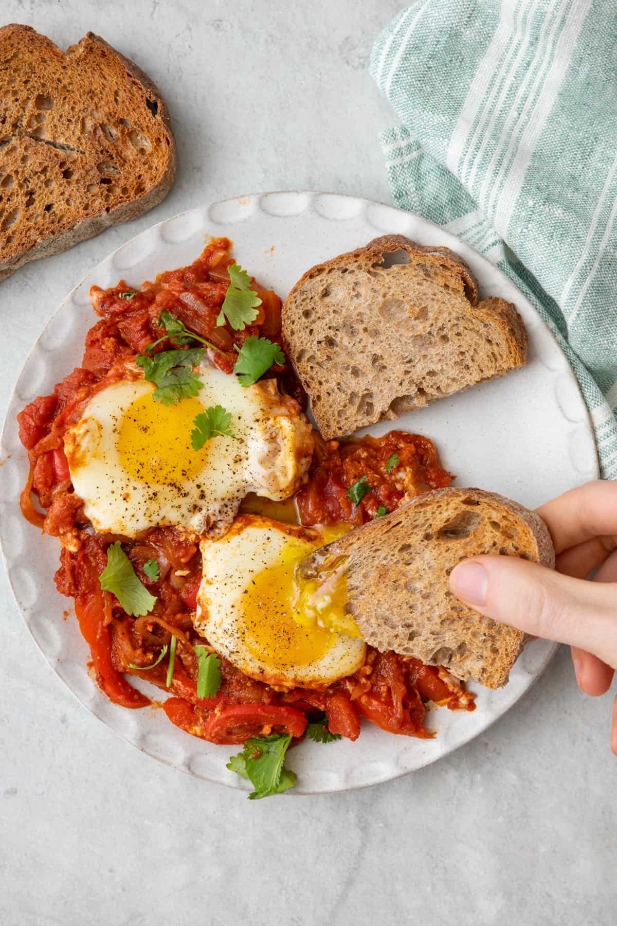 A nutritious dish featuring poached eggs in a spiced tomato sauce, served with whole grain bread and garnished with fresh cilantro.