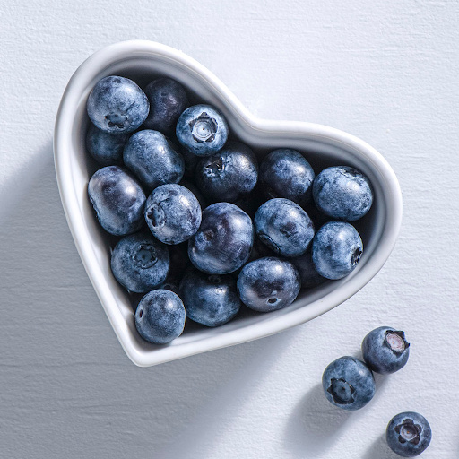 A heart-shaped bowl filled with fresh blueberries, a low-calorie fruit rich in antioxidants and nutrients.