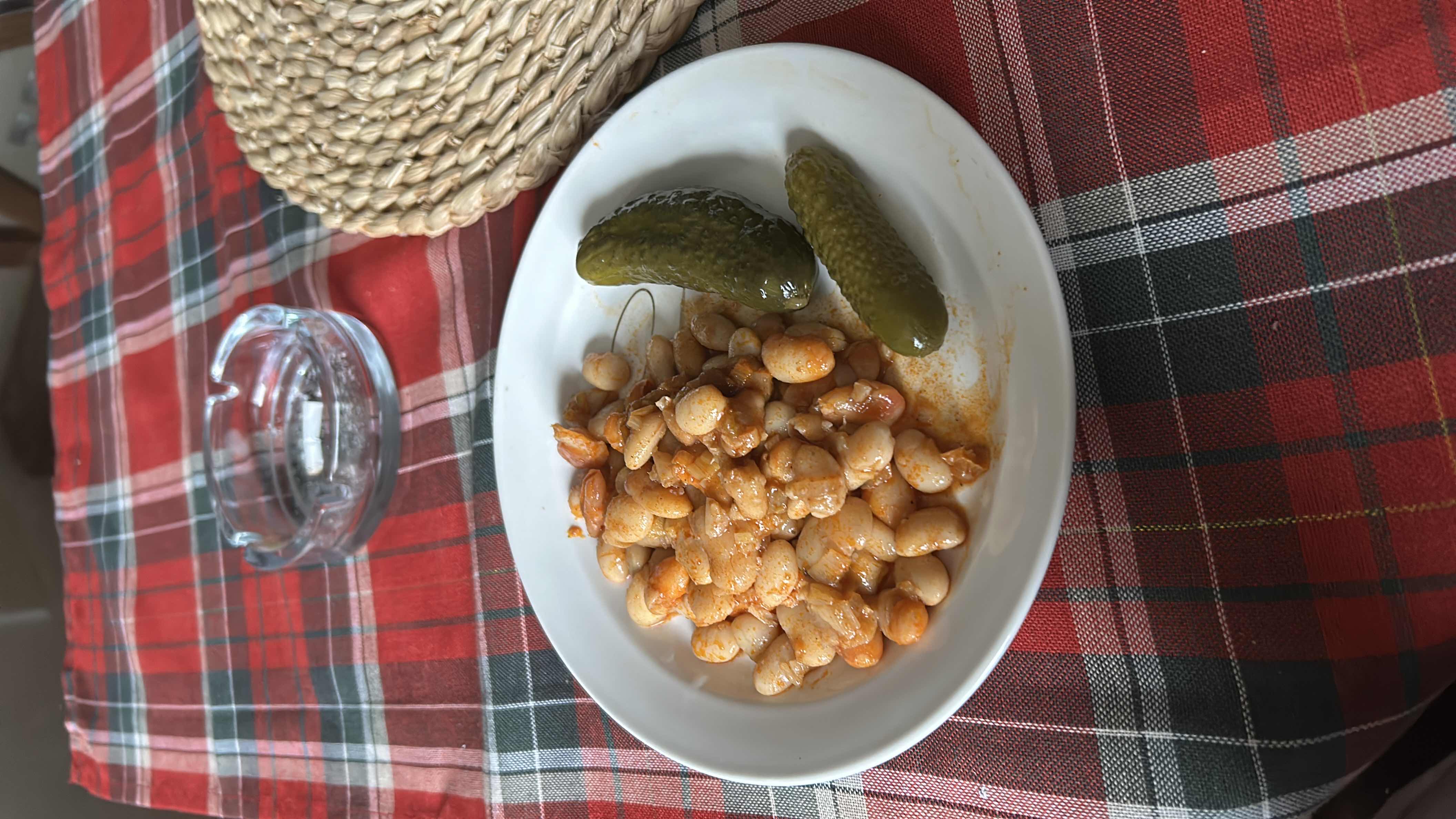 A plate of cooked beans with a light sauce, accompanied by pickles, providing a balanced and nutritious meal.