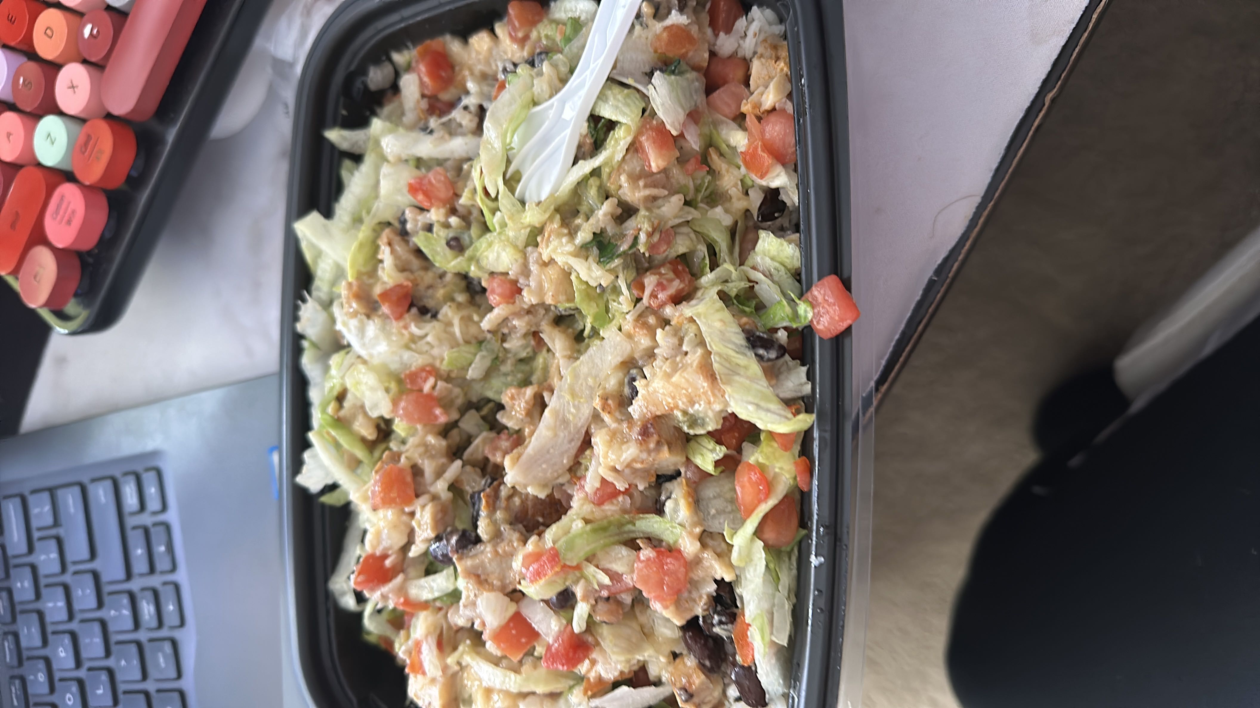 A healthy salad with lettuce, free bird chicken, tomatoes, black beans, cheese, and dressing, providing a balanced mix of protein, carbs, and fats.
