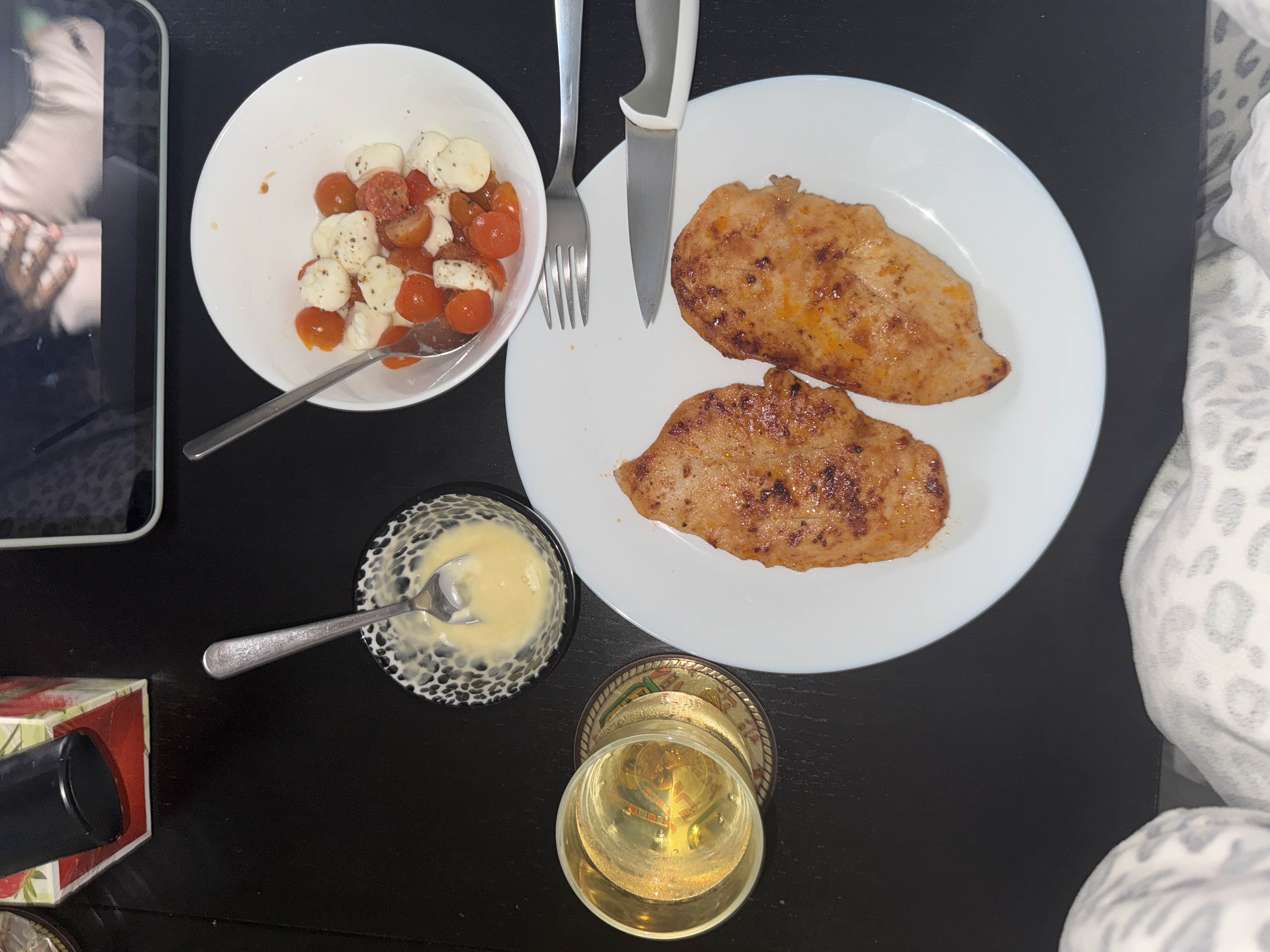 A meal consisting of grilled chicken breast, a side of cherry tomatoes with mozzarella, and a small portion of dressing.
