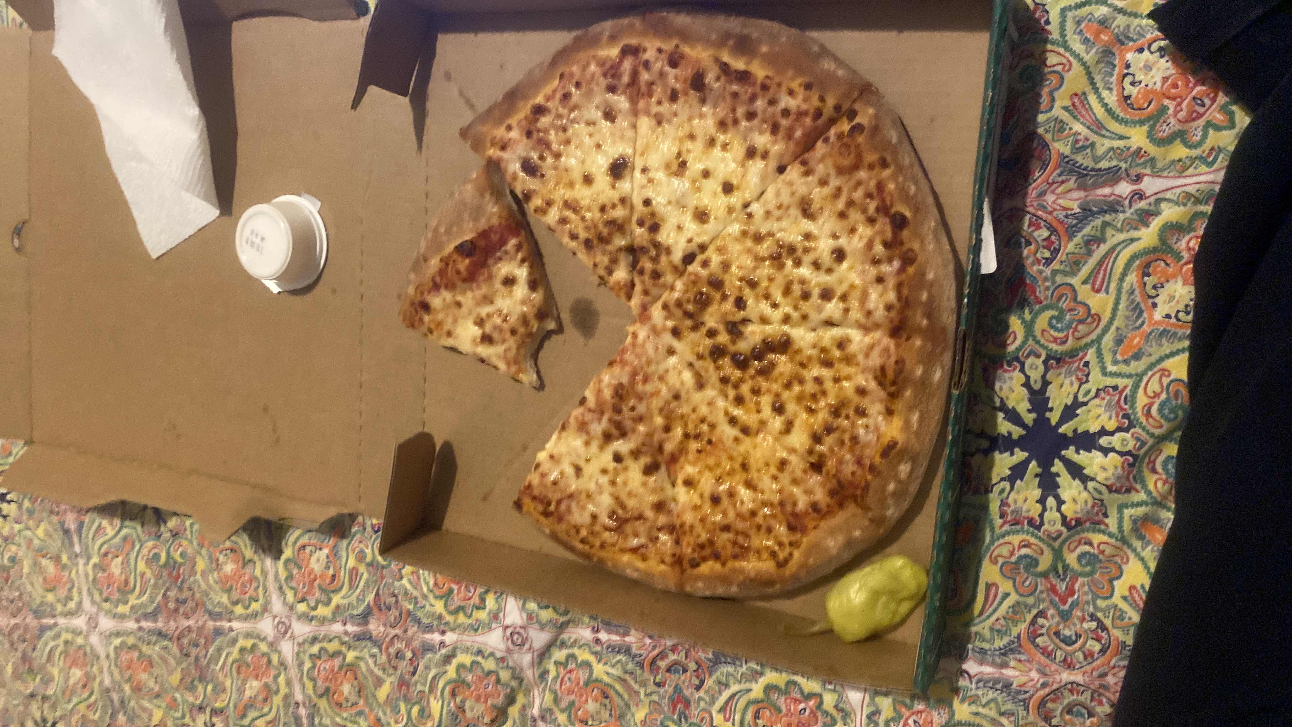 A cheese pizza with a side of pepperoncini, featuring a crispy crust and tomato sauce.