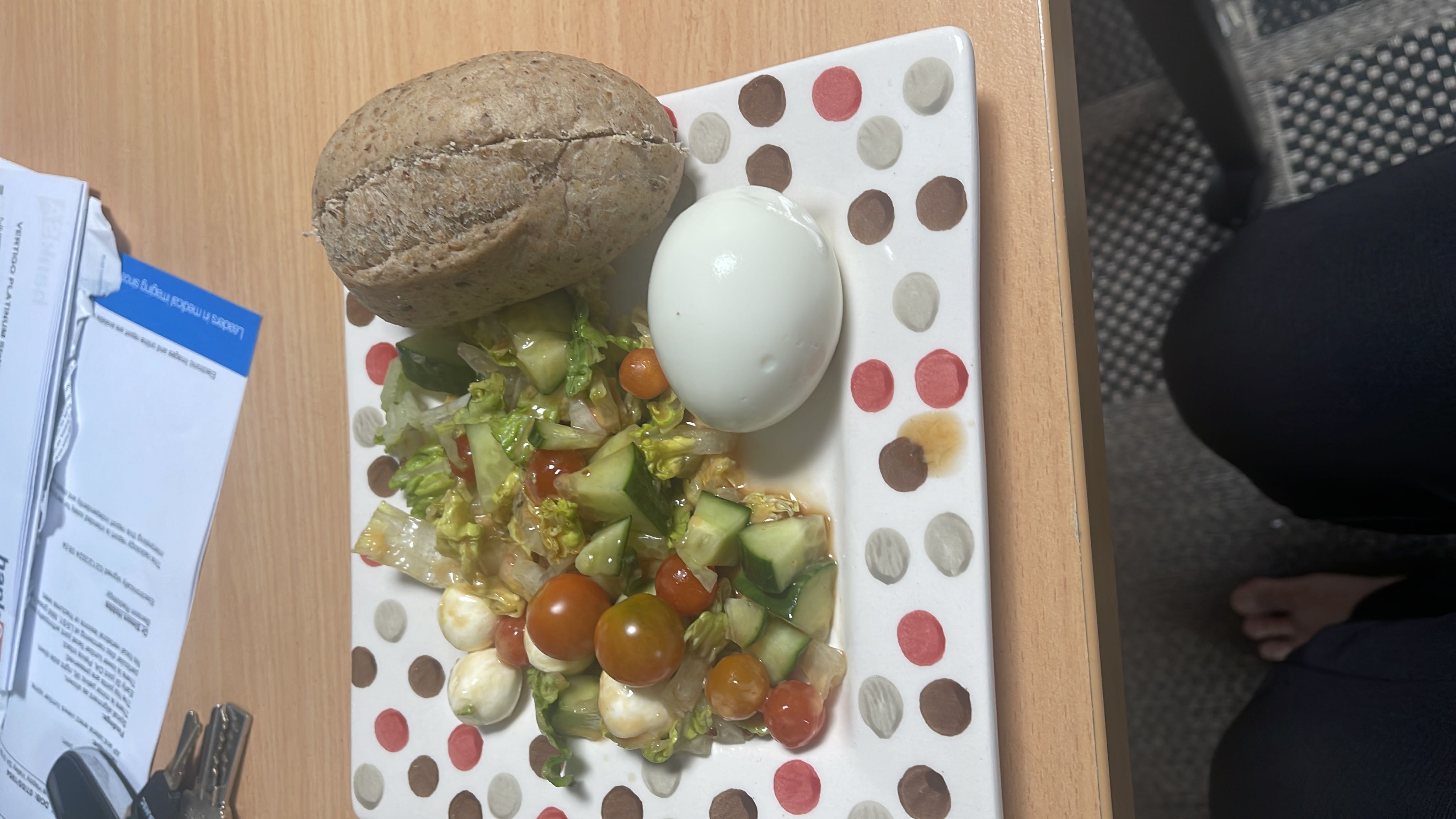 A balanced meal consisting of a boiled egg, whole grain bread, and a fresh salad with lettuce, cucumber, cherry tomatoes, and mozzarella.