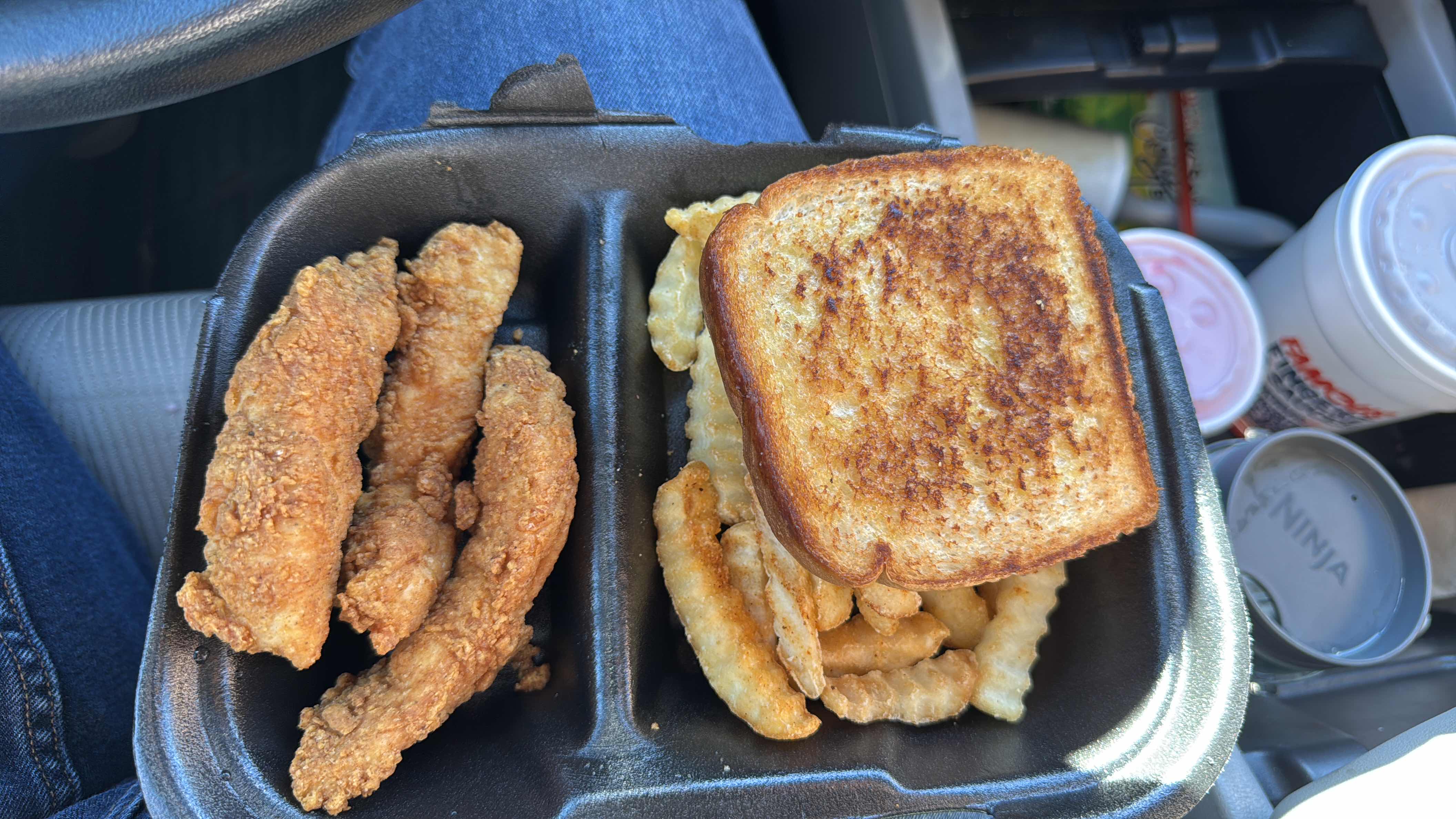 A meal consisting of fried chicken tenders, crinkle-cut fries, and a slice of toasted bread.