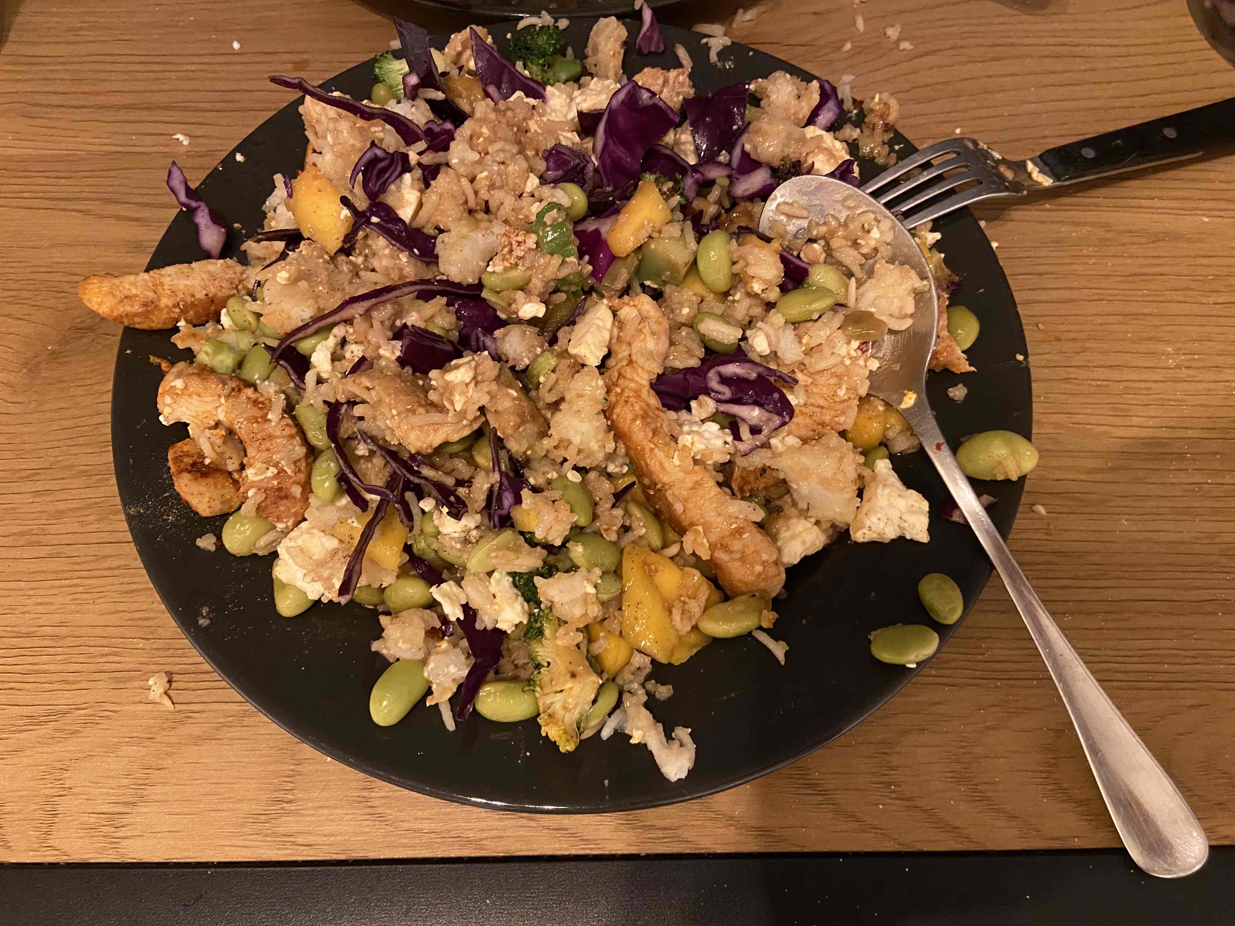 A healthy dish consisting of chicken, edamame, red cabbage, mango, and cauliflower rice, providing a balanced mix of protein, carbs, and fats.