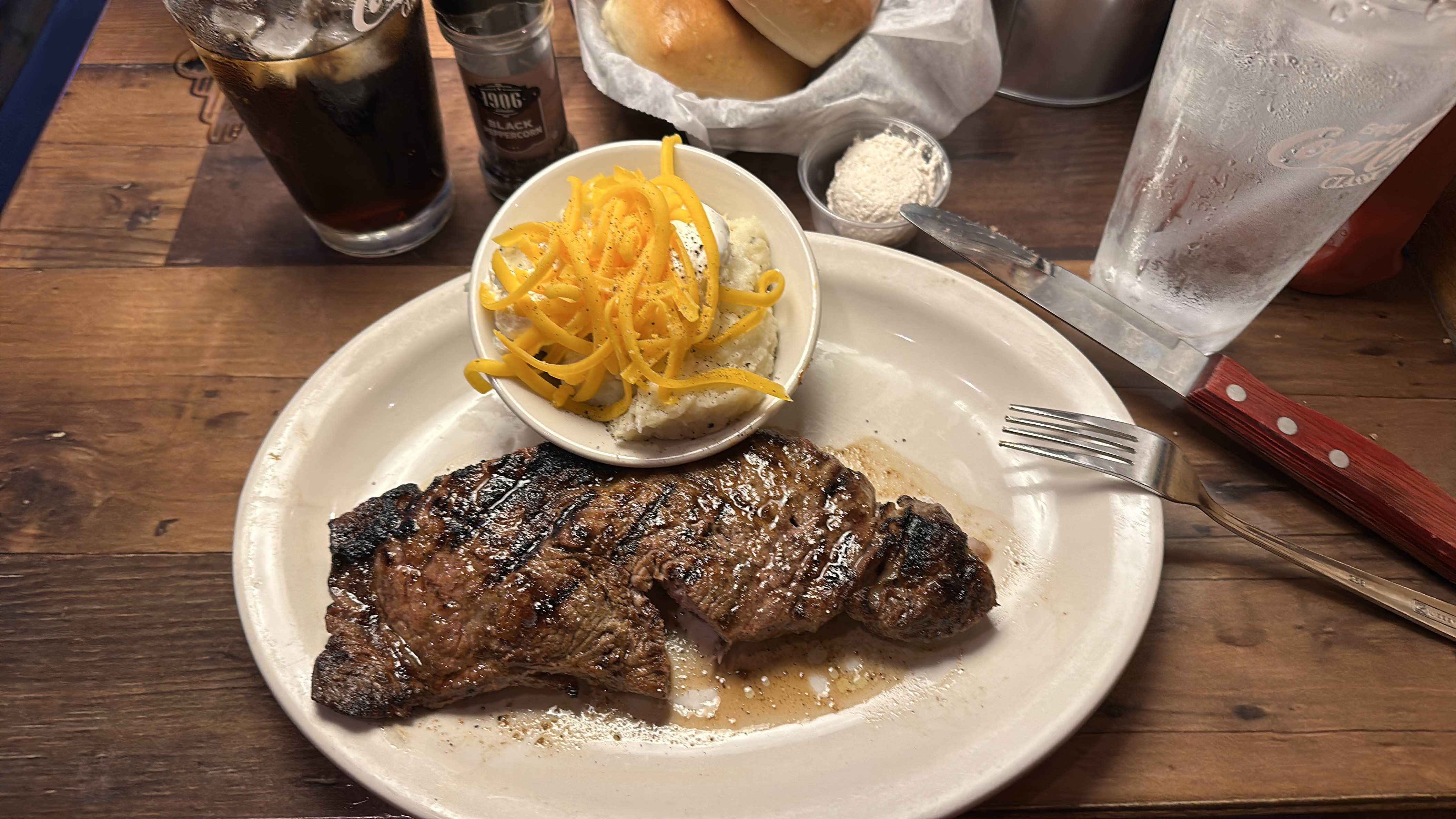 A hearty meal consisting of a grilled steak, mashed potatoes topped with cheese, and a dinner roll.