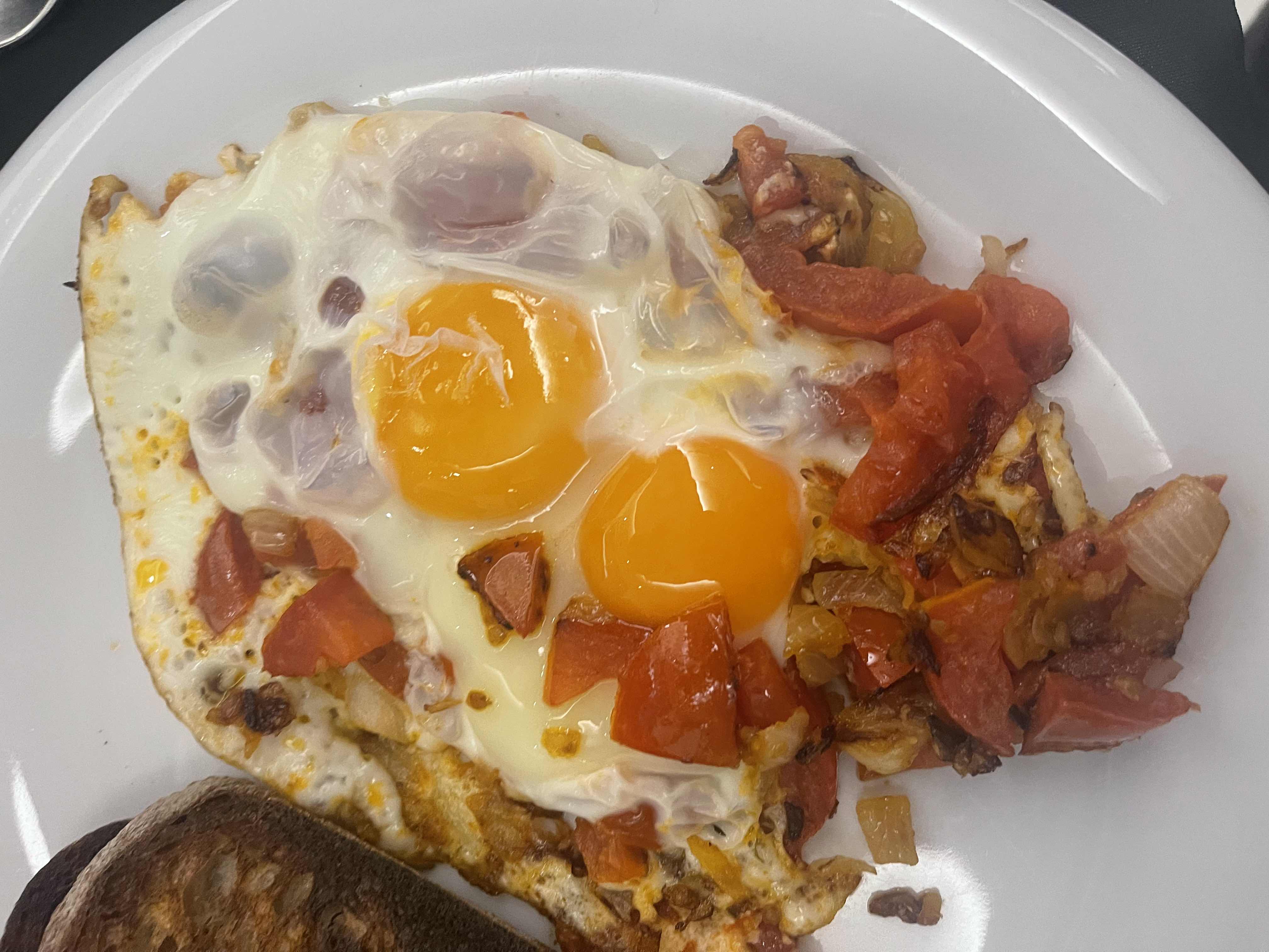 A dish consisting of fried eggs served with sautéed tomatoes, onions, and a side of toast.