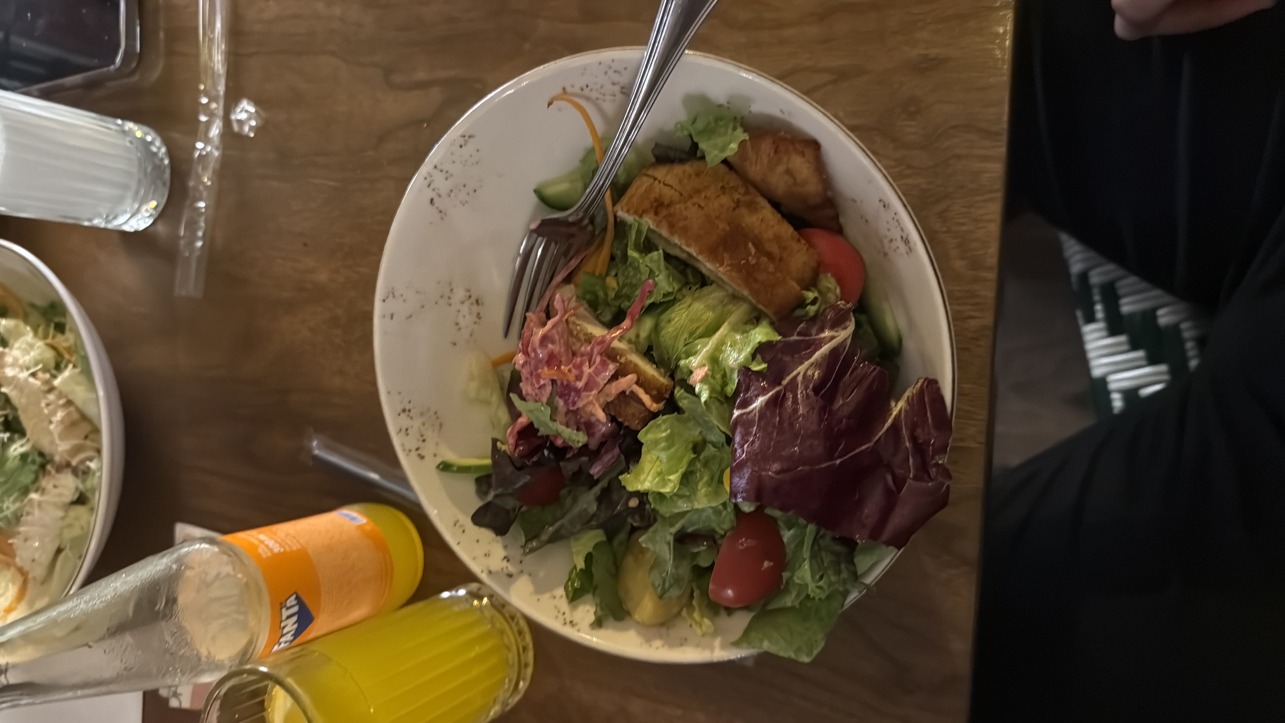 A healthy salad bowl containing lettuce, cherry tomatoes, grilled chicken, carrots, cucumber, and dressing, served with a side of orange soda.