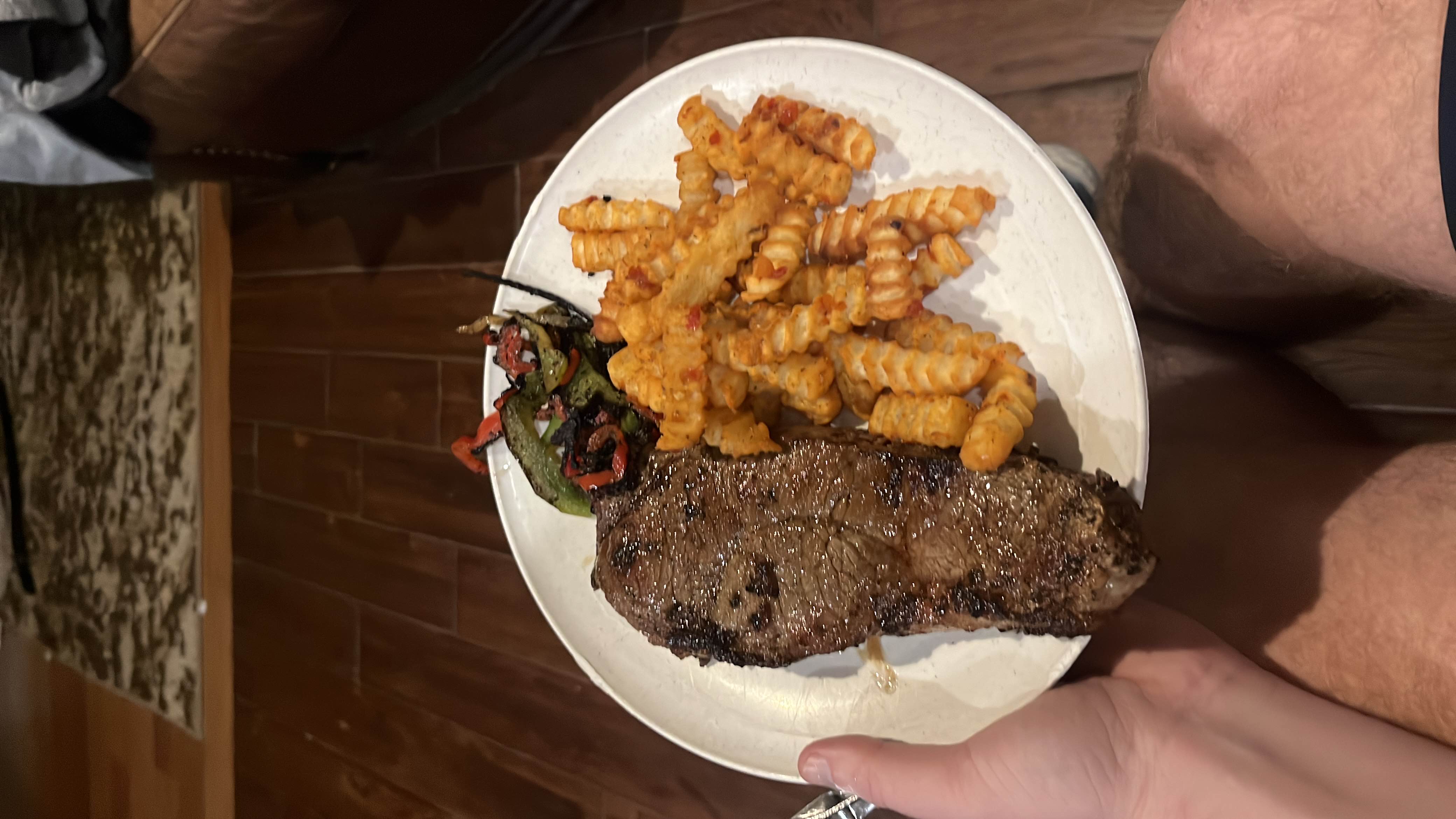 A plate containing a grilled steak, crinkle-cut fries, and a side of grilled vegetables.