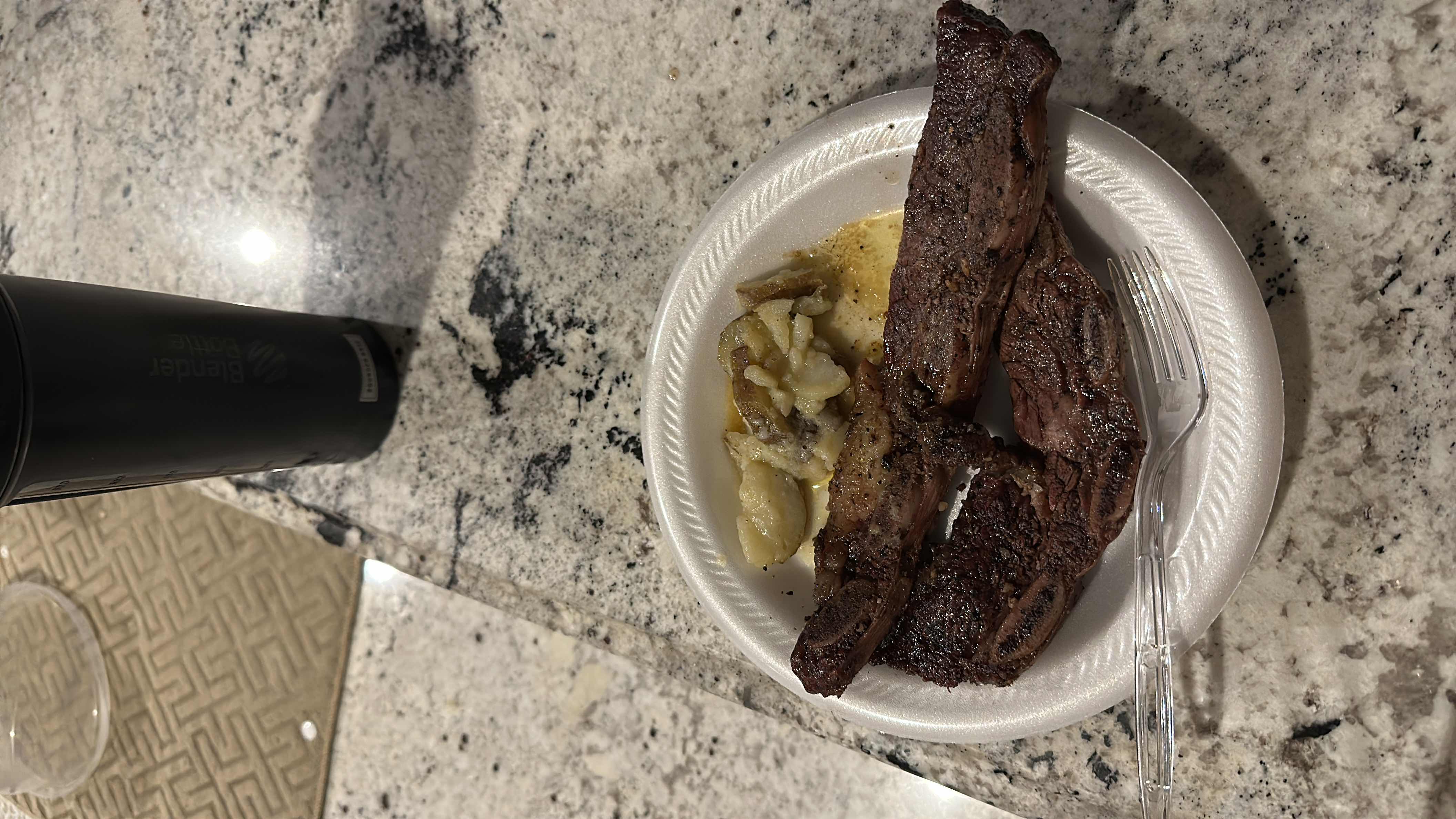 A meal consisting of grilled beef and mashed potatoes, served on a disposable plate.