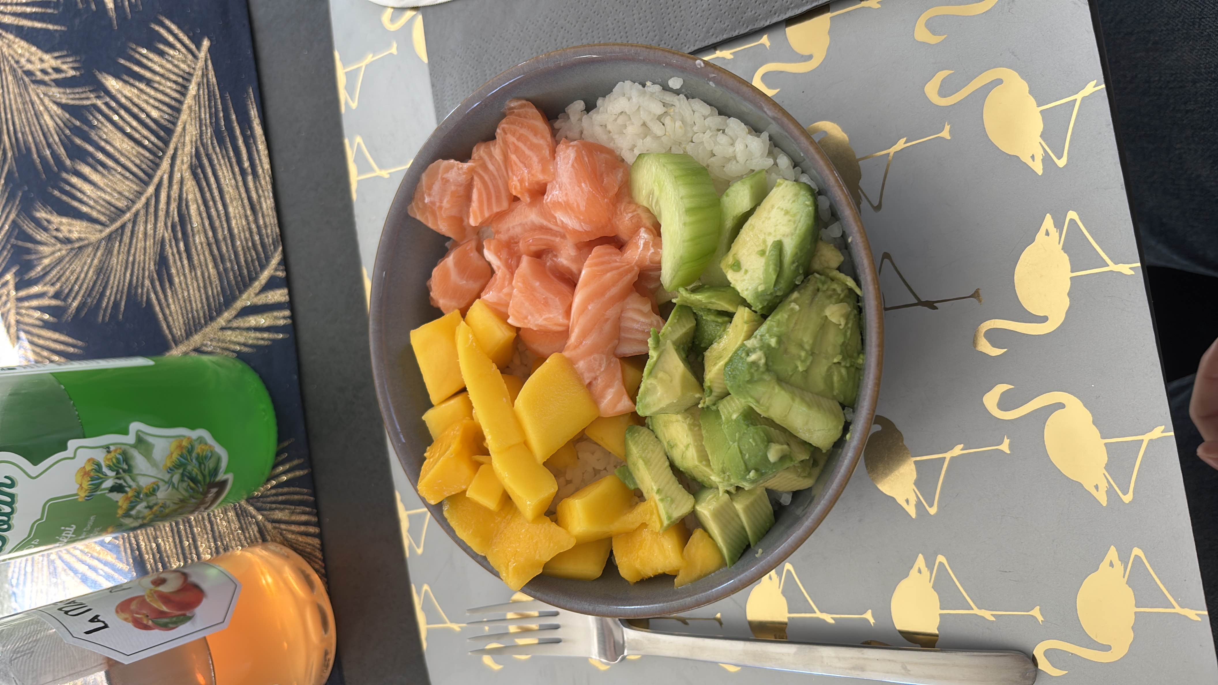 A nutritious poke bowl containing salmon, mango, avocado, cucumber, and rice, offering a balanced mix of protein, carbs, and healthy fats.