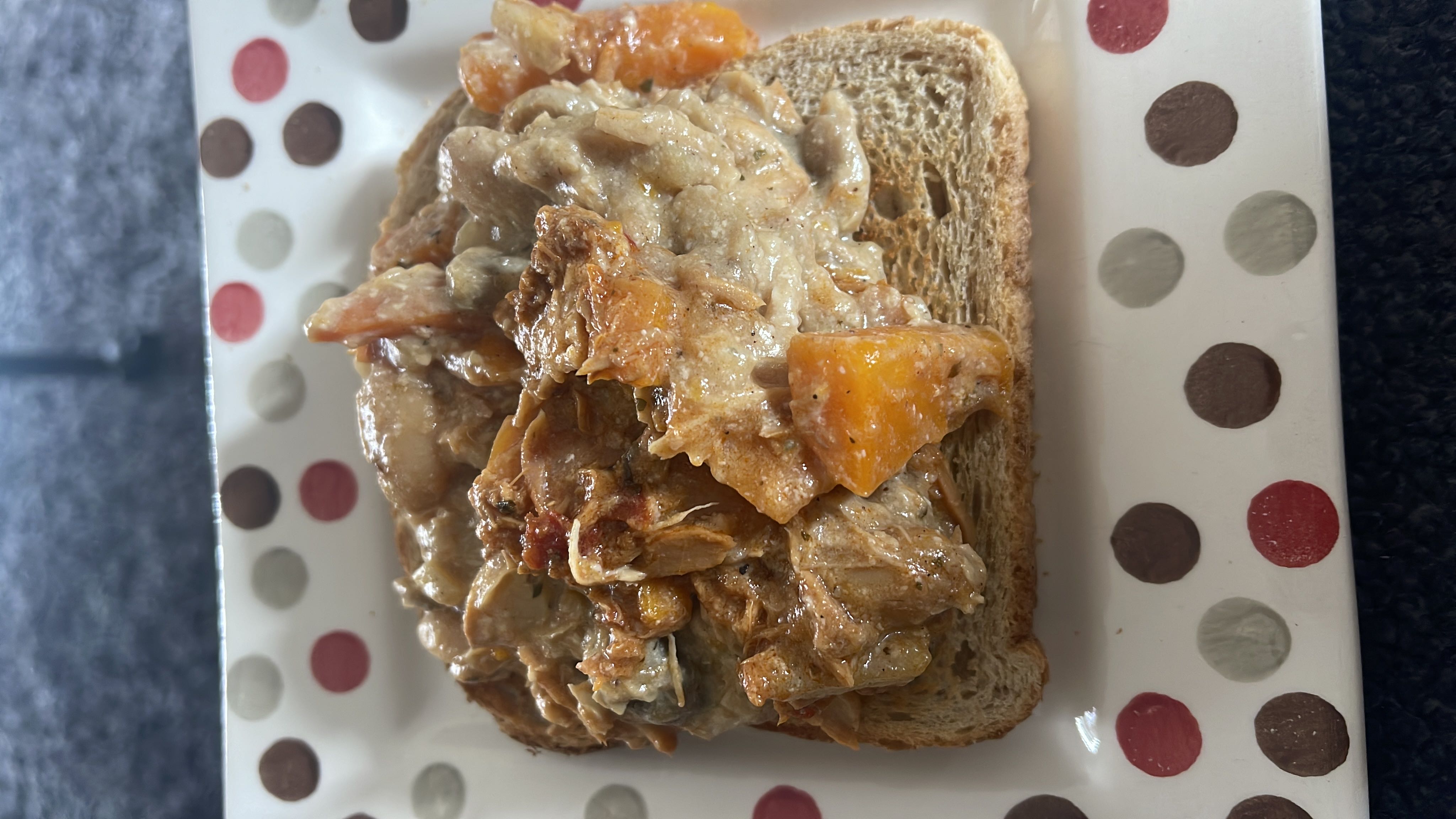 An open-faced sandwich with a creamy chicken and vegetable topping served on a slice of bread.