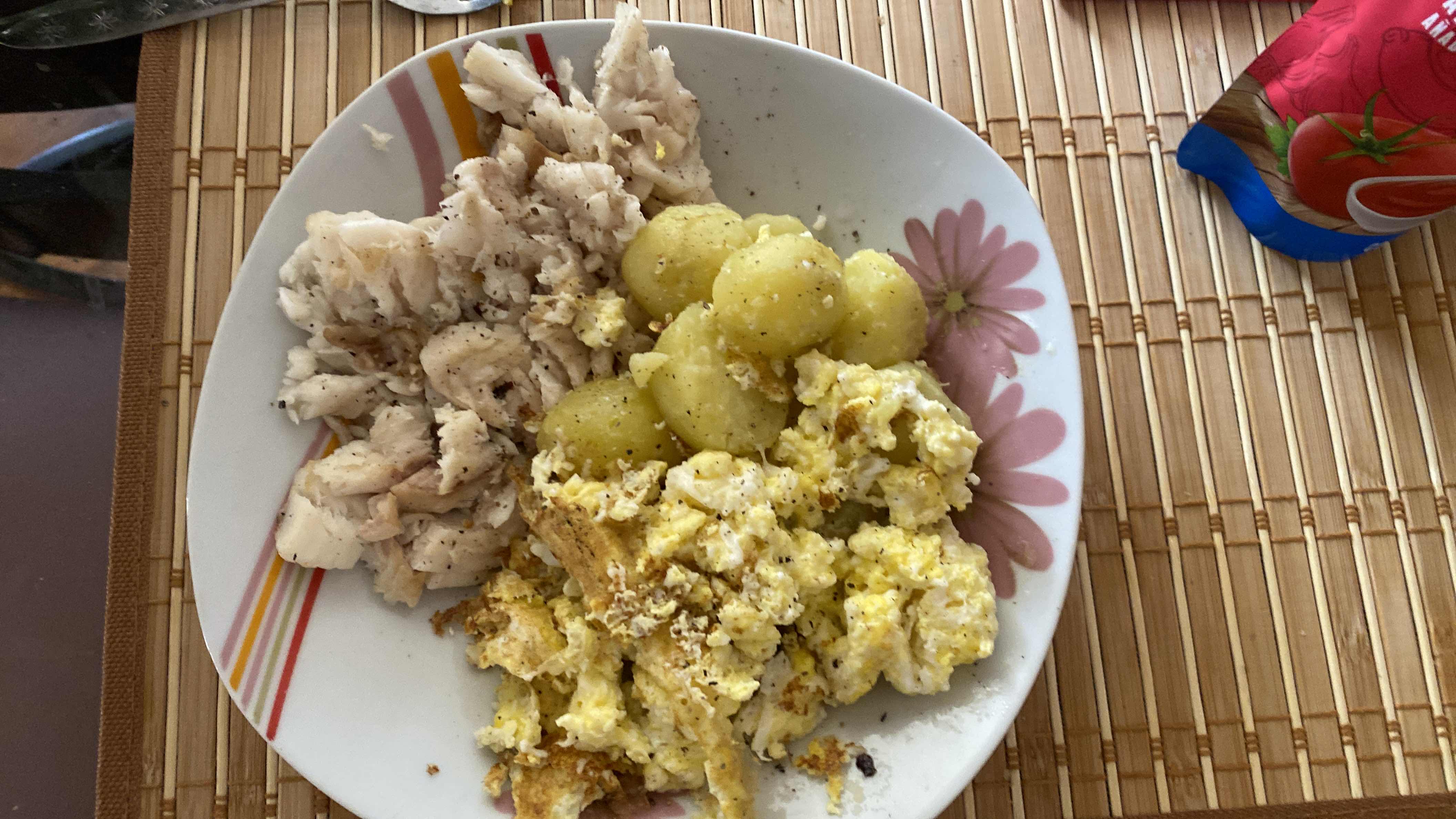 A balanced meal consisting of scrambled eggs, boiled potatoes, and cooked fish, providing a good mix of protein, carbs, and fats.