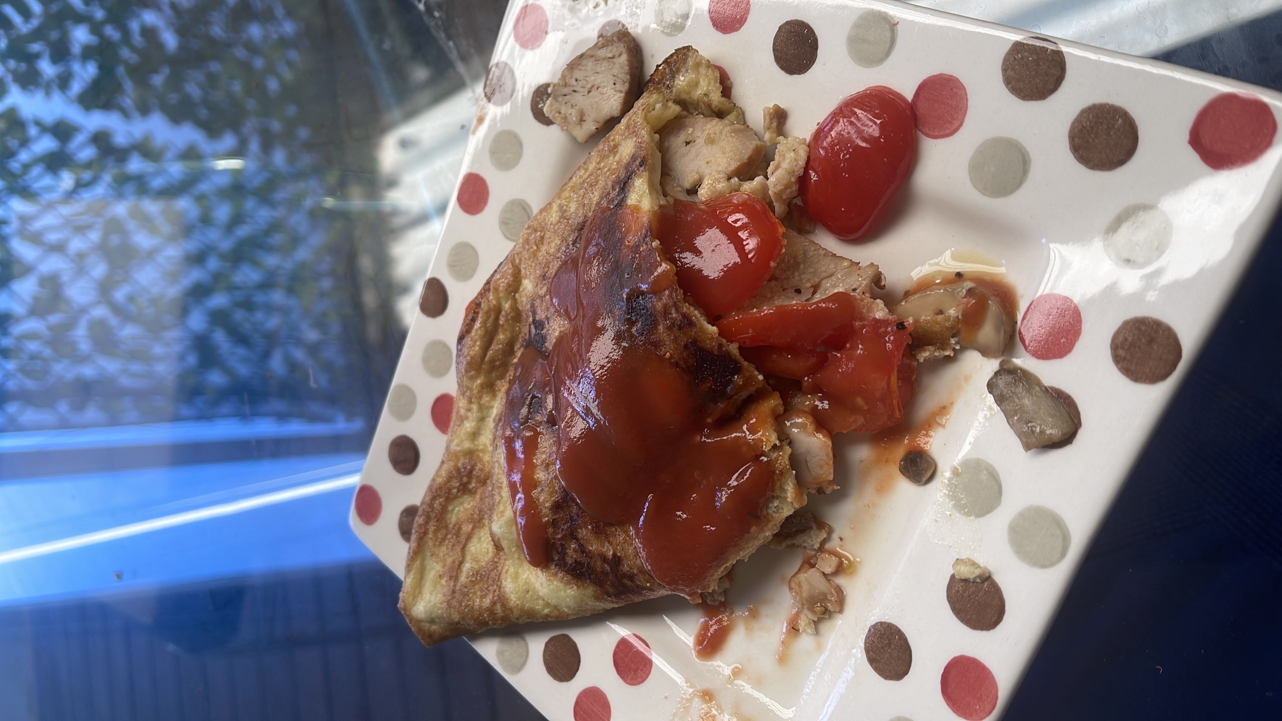 An omelette filled with chicken, tomatoes, mushrooms, and topped with ketchup, providing a balanced mix of protein, carbs, and fats.
