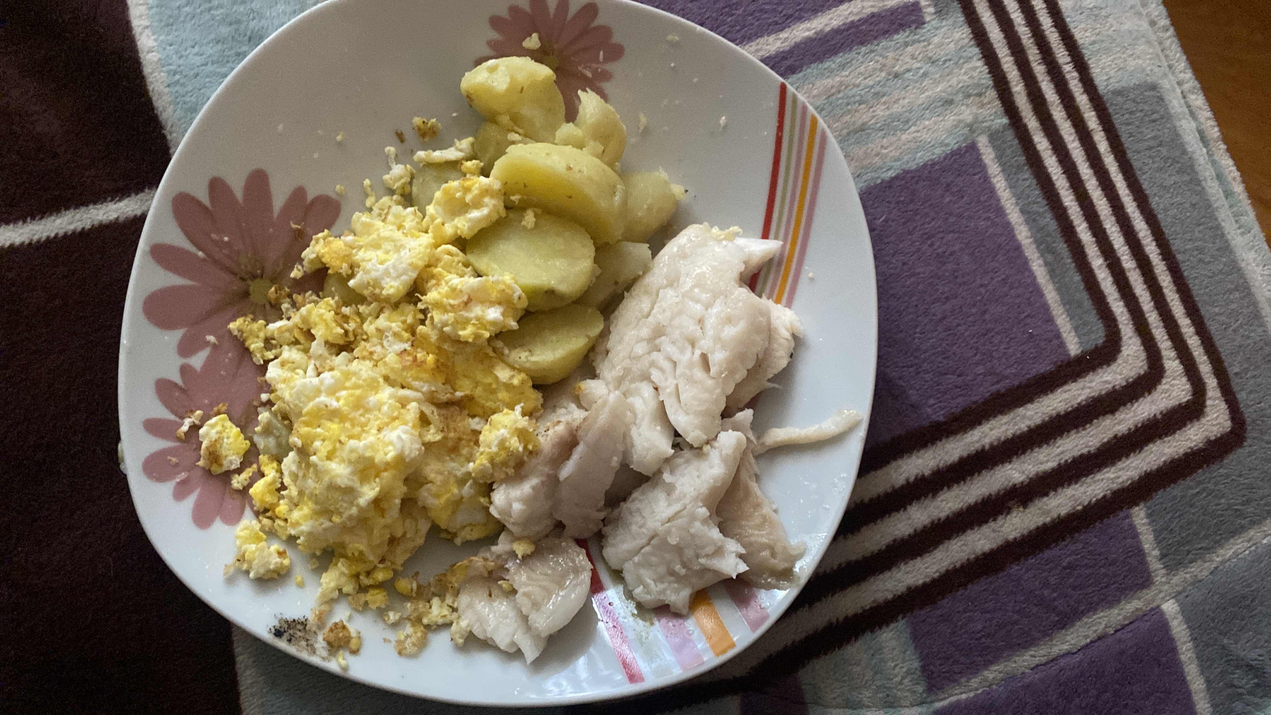 A plate containing scrambled eggs, boiled potatoes, and boiled fish, providing a balanced meal with moderate calories and a good protein source.