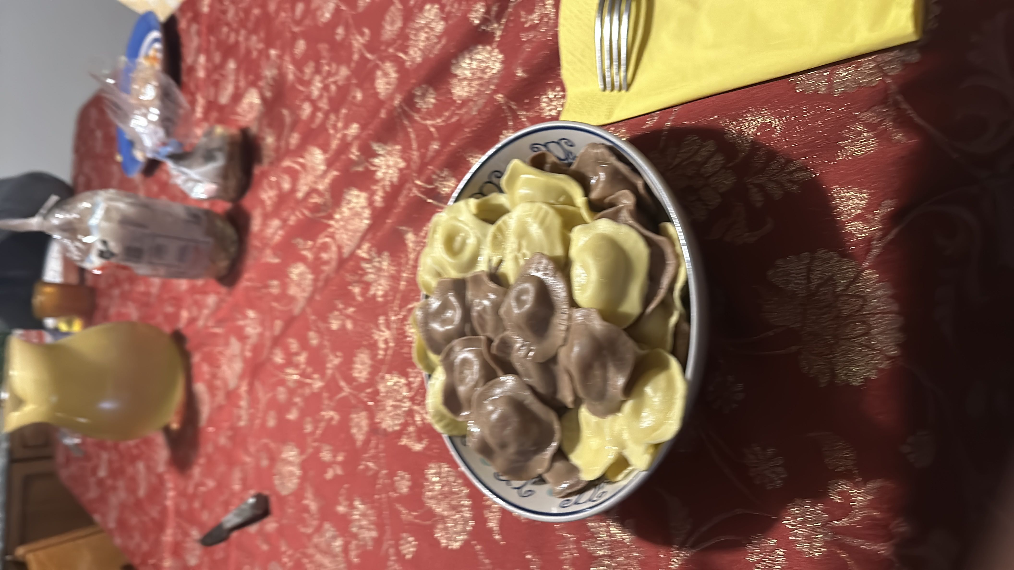 A bowl of cheese-filled ravioli, featuring both plain and cocoa-infused pasta shells, served on a decorative table setting.