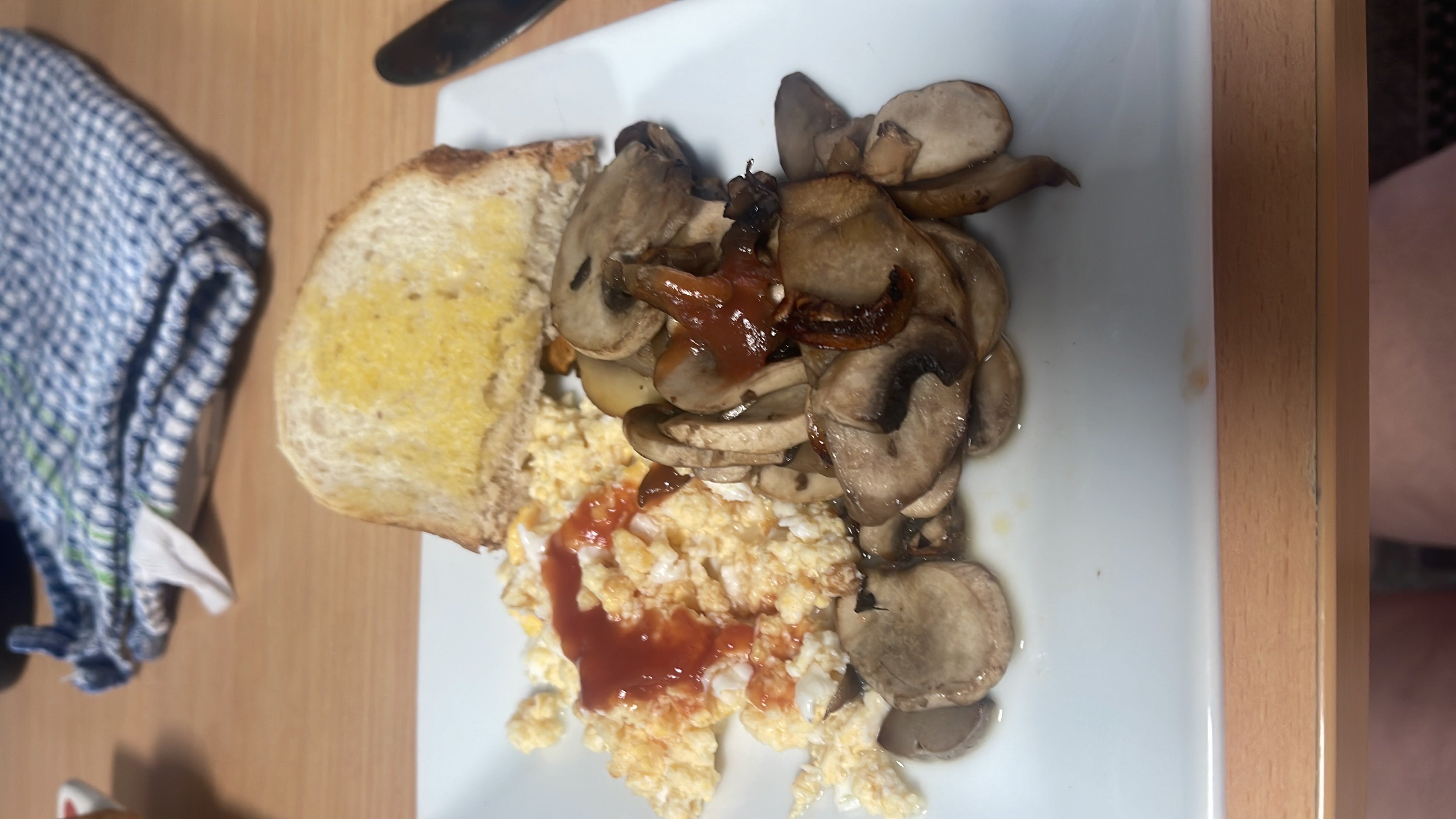 A balanced meal consisting of scrambled eggs with ketchup, sautéed mushrooms, and buttered toast.