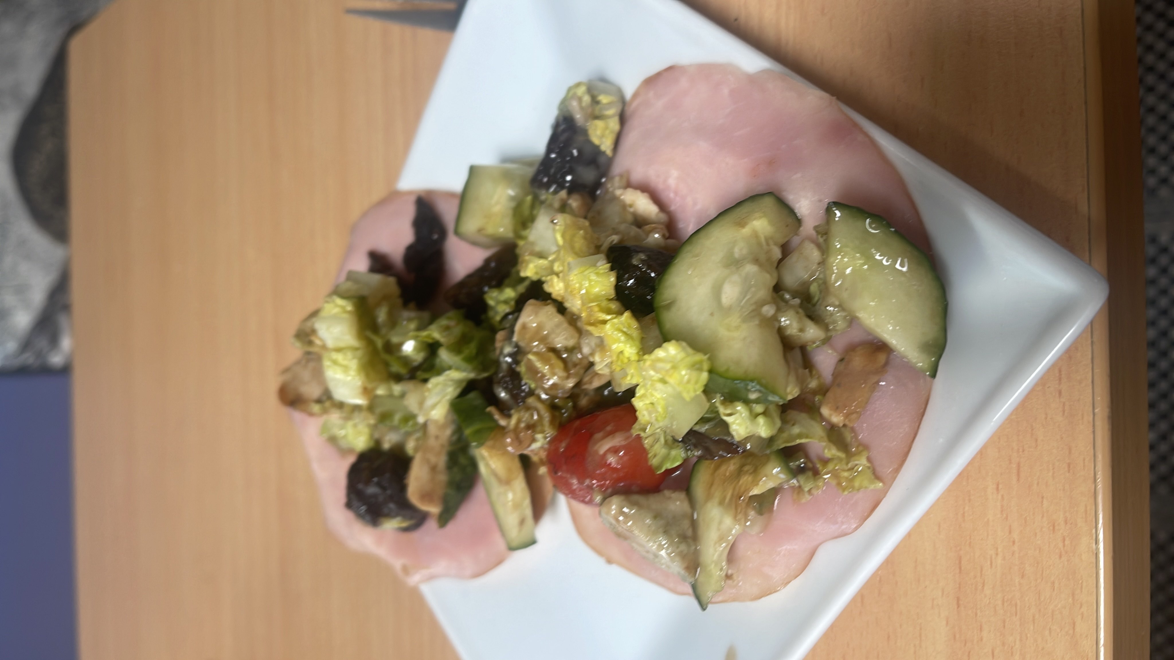 A light and healthy dish featuring ham slices topped with a fresh salad of lettuce, cucumber, cherry tomatoes, walnuts, and a light dressing.