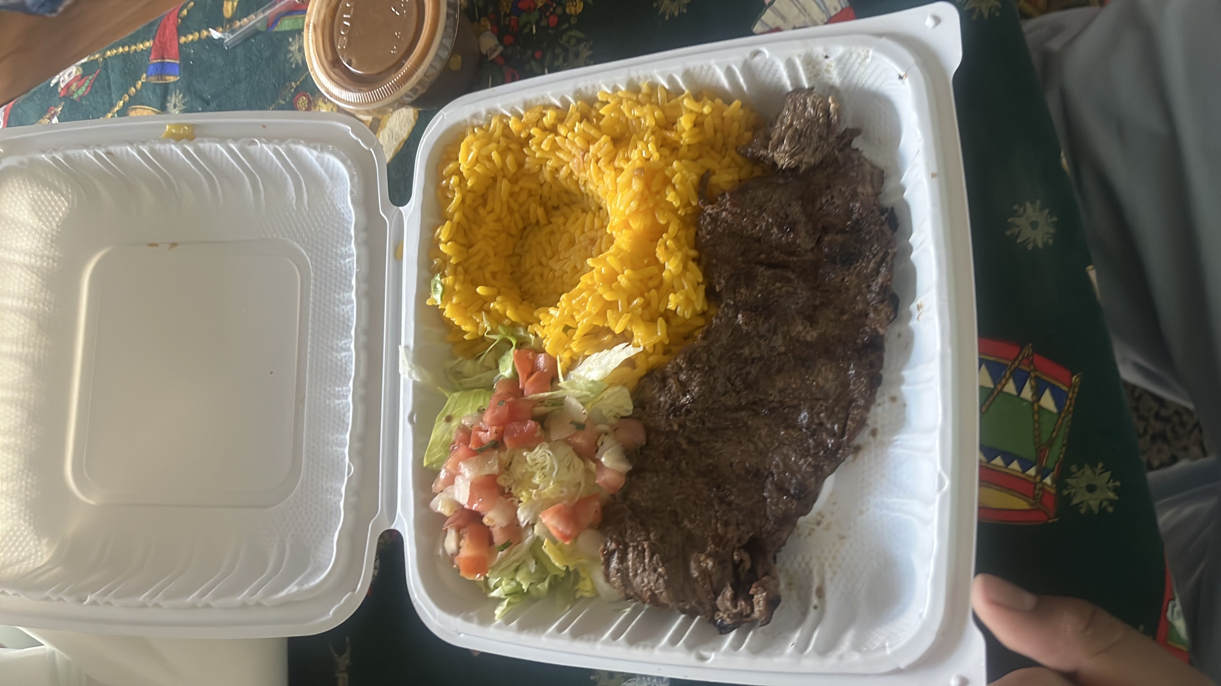 A meal consisting of grilled steak, yellow rice, and a side salad with tomatoes, accompanied by a dressing.