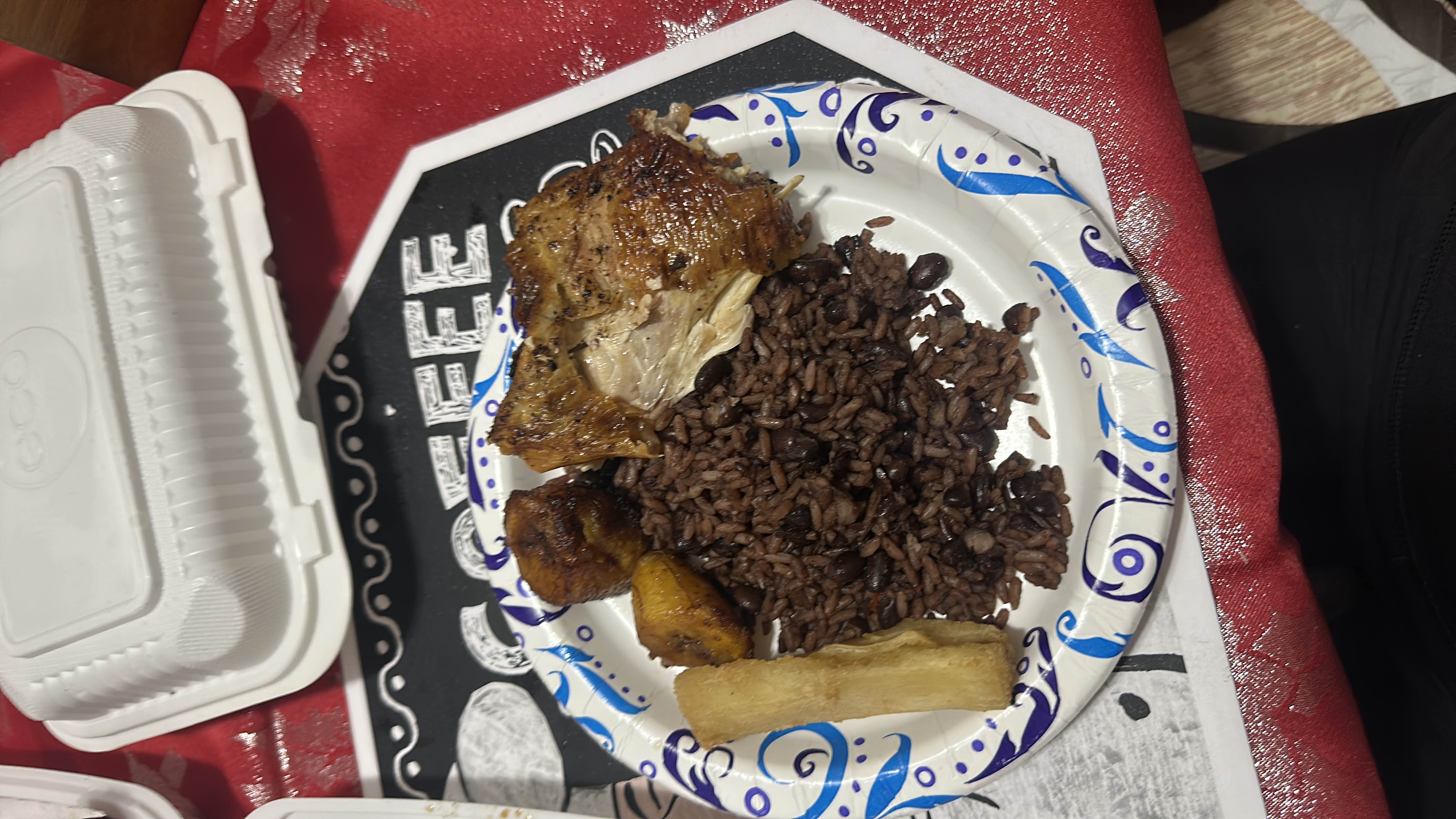 A plate featuring roasted chicken, rice with black beans, fried plantains, and yuca.