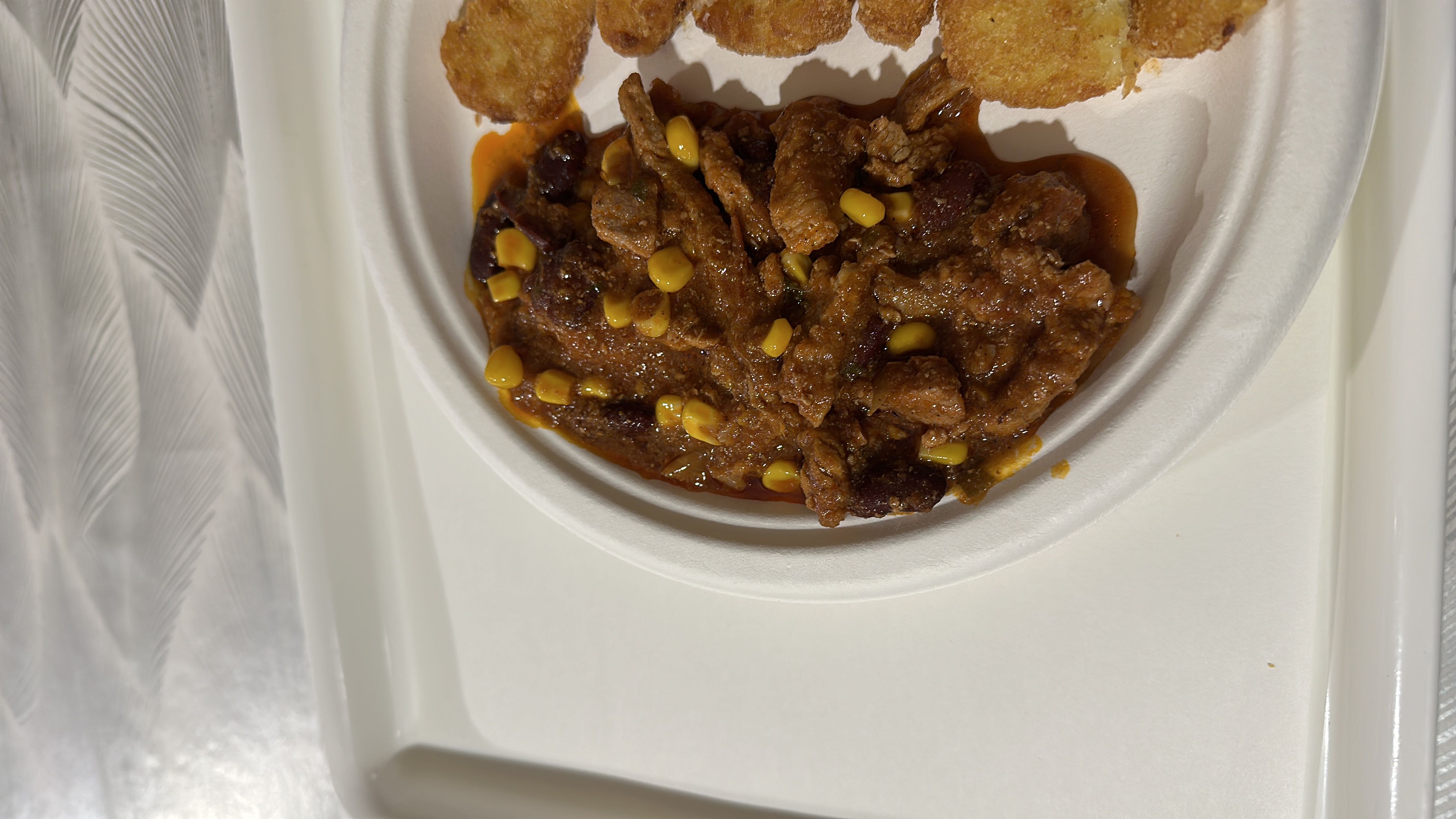 A chili-style dish with beef, beans, corn, and fried potato bites.