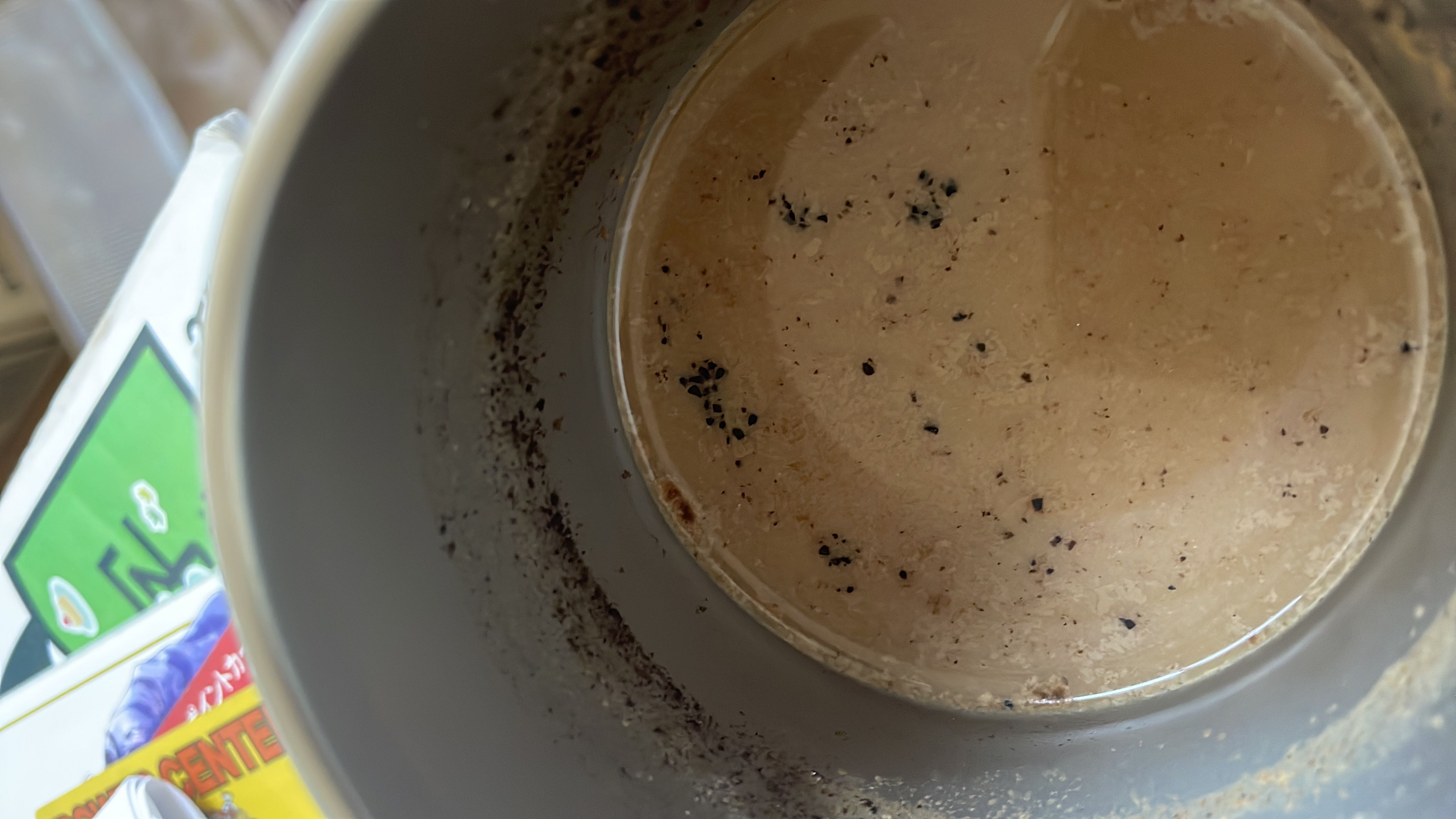 A cup containing a lightly creamed coffee beverage with small coffee grounds visible.