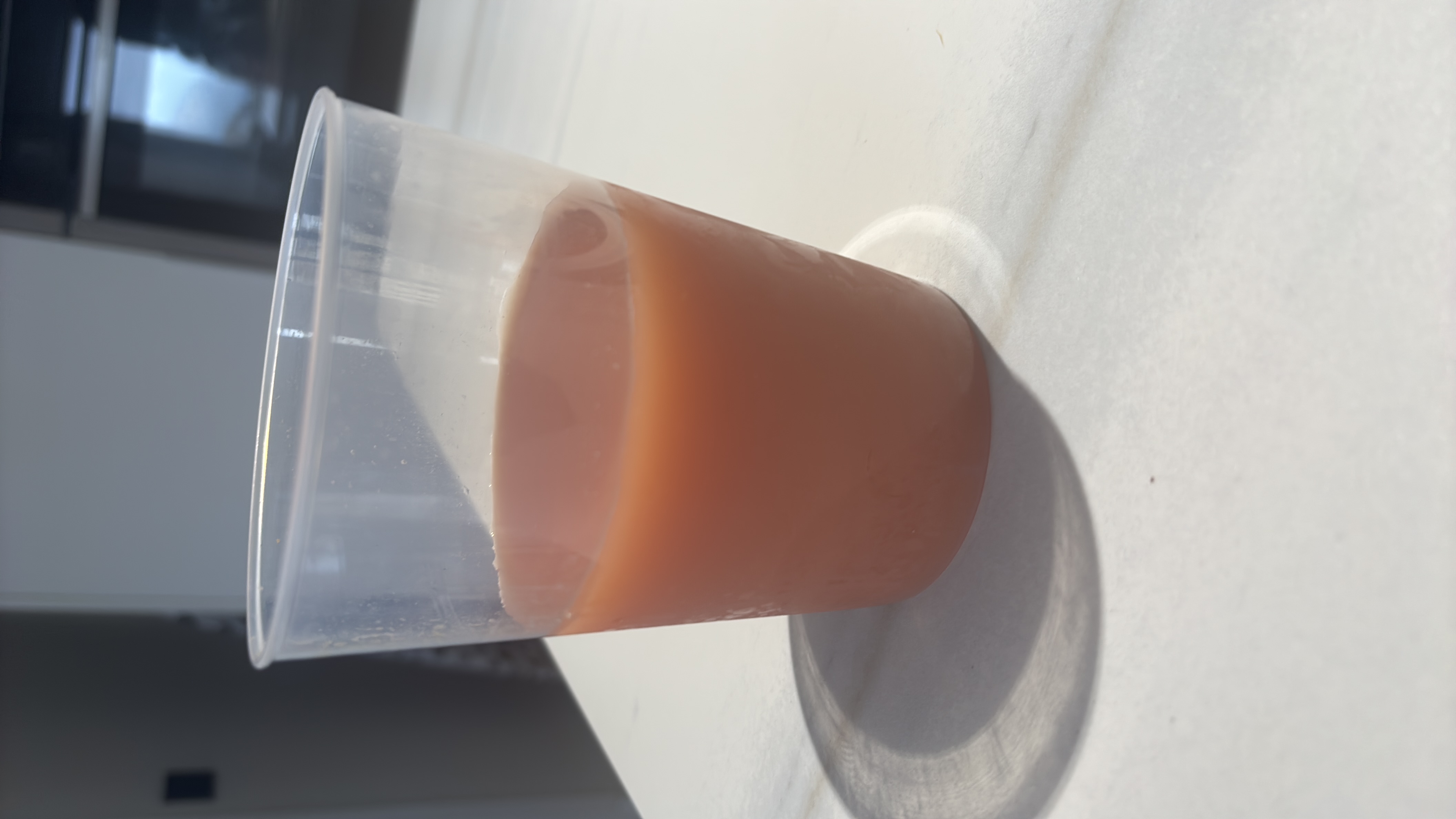 A plastic cup containing a pinkish-orange juice with moderate carbohydrate content and low protein and fat.