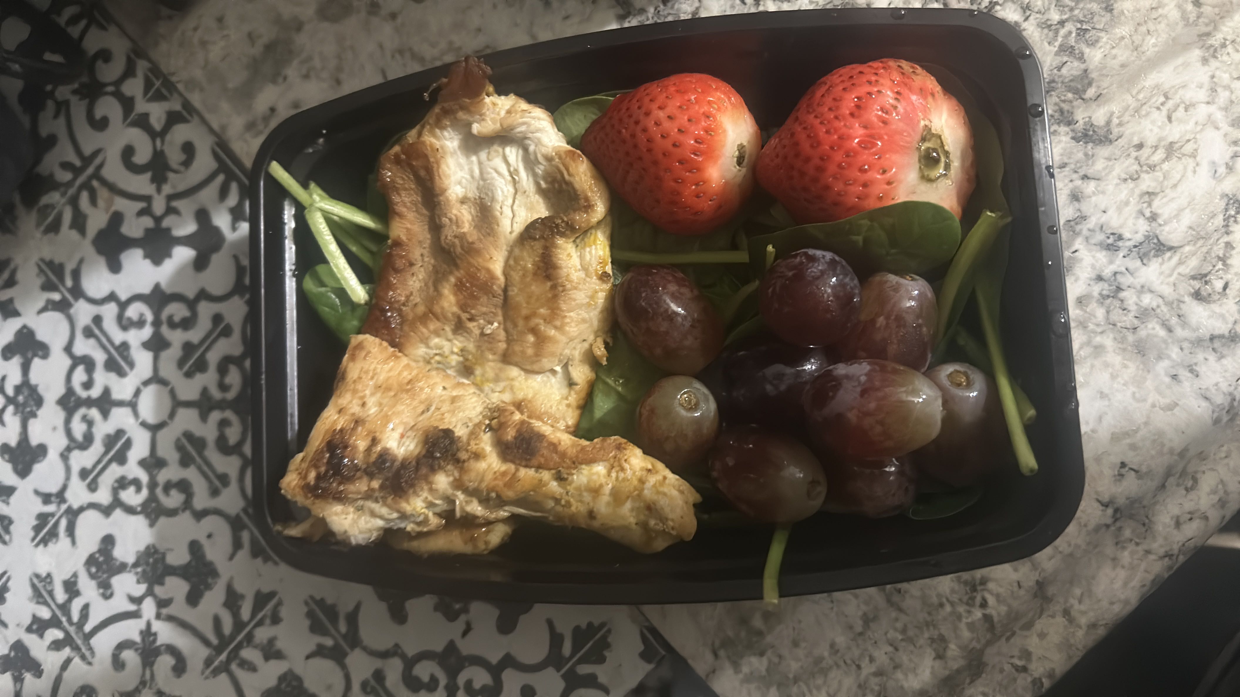 A balanced meal with grilled chicken, spinach, grapes, and strawberries.