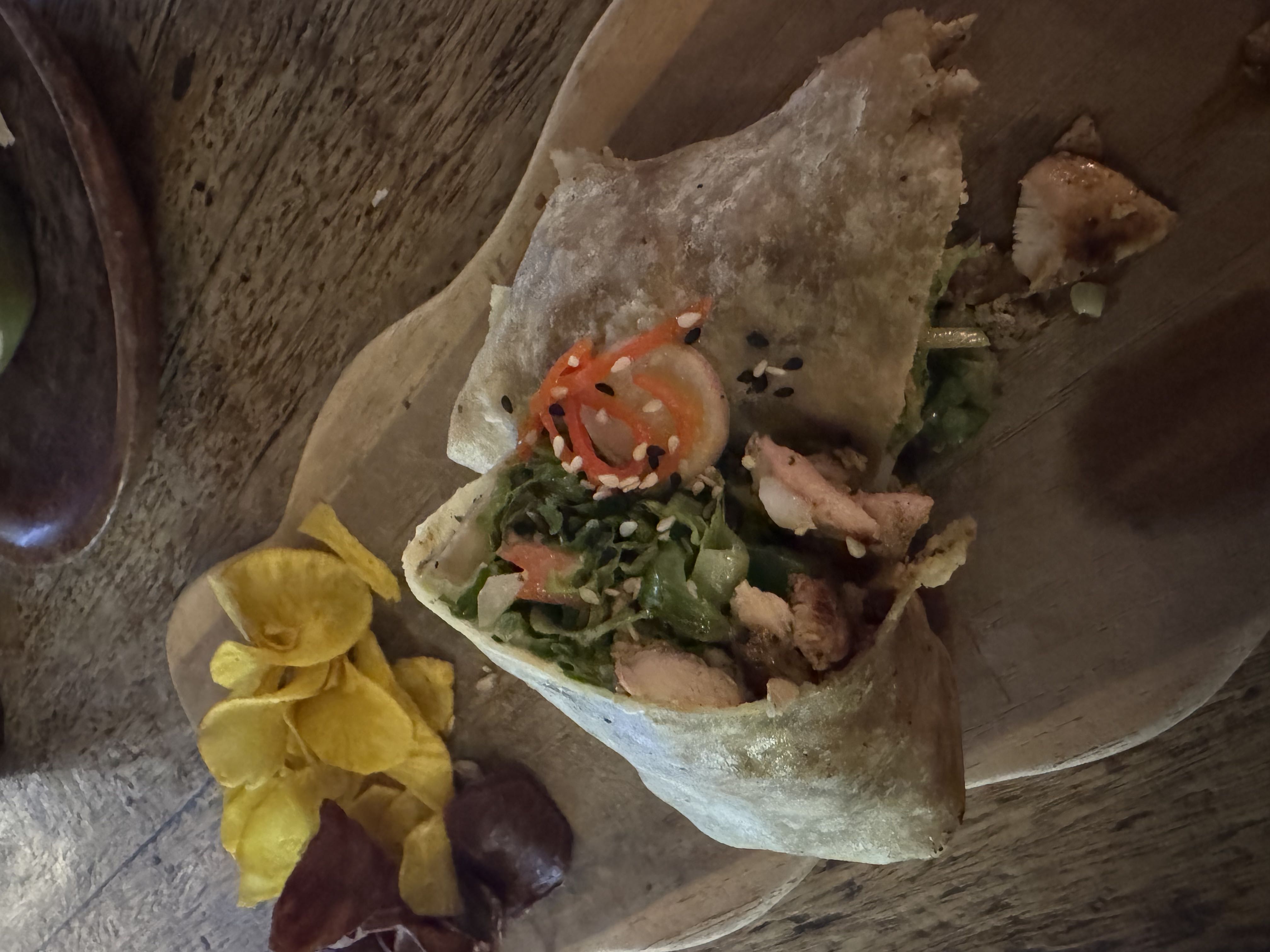 A wrap filled with chicken, fresh vegetables, and sesame seeds, served with a side of vegetable chips.
