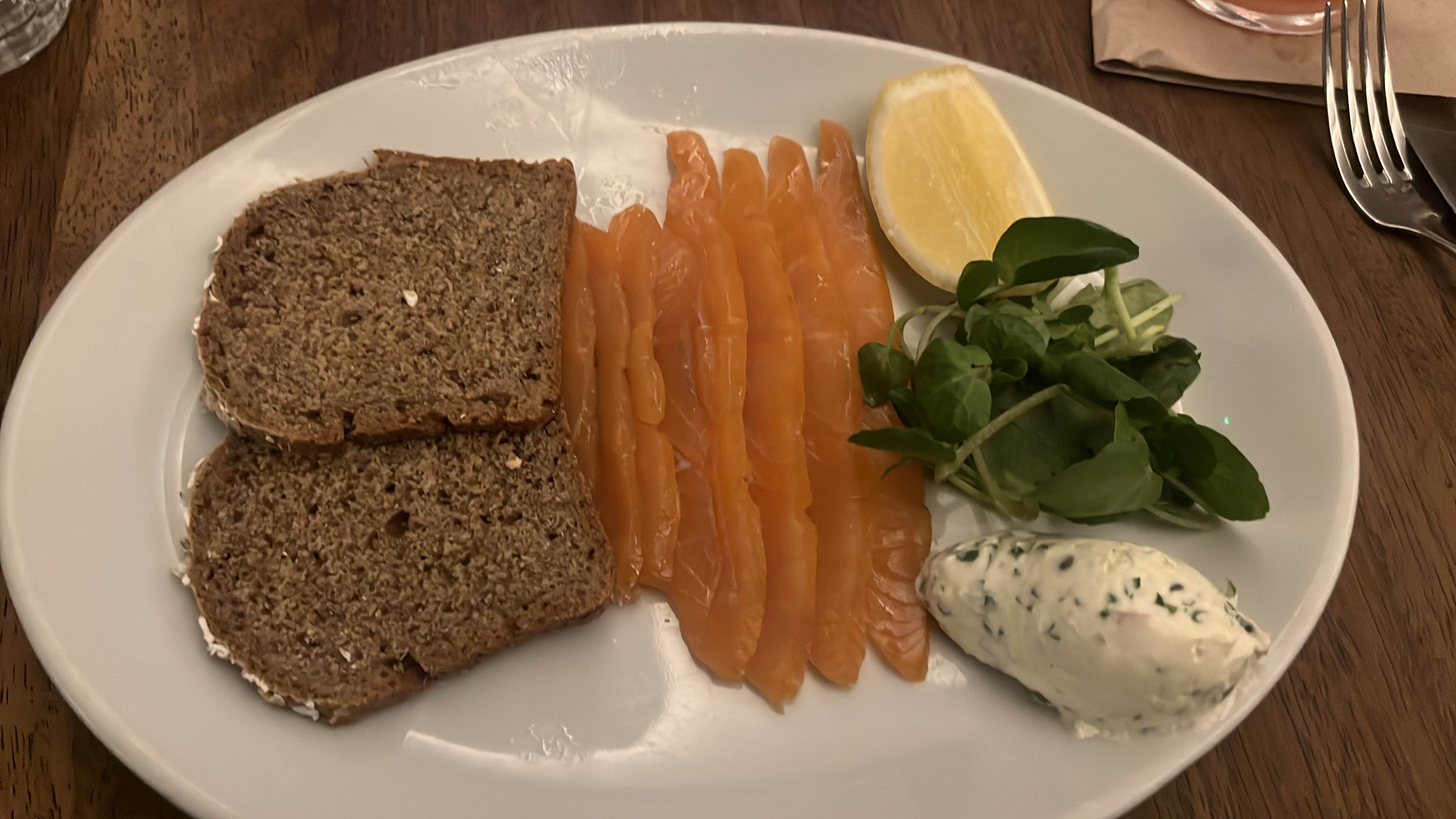 A balanced meal featuring rye bread, smoked salmon, herbed cream cheese, watercress, and a lemon wedge, providing a good mix of protein, carbs, and fats.