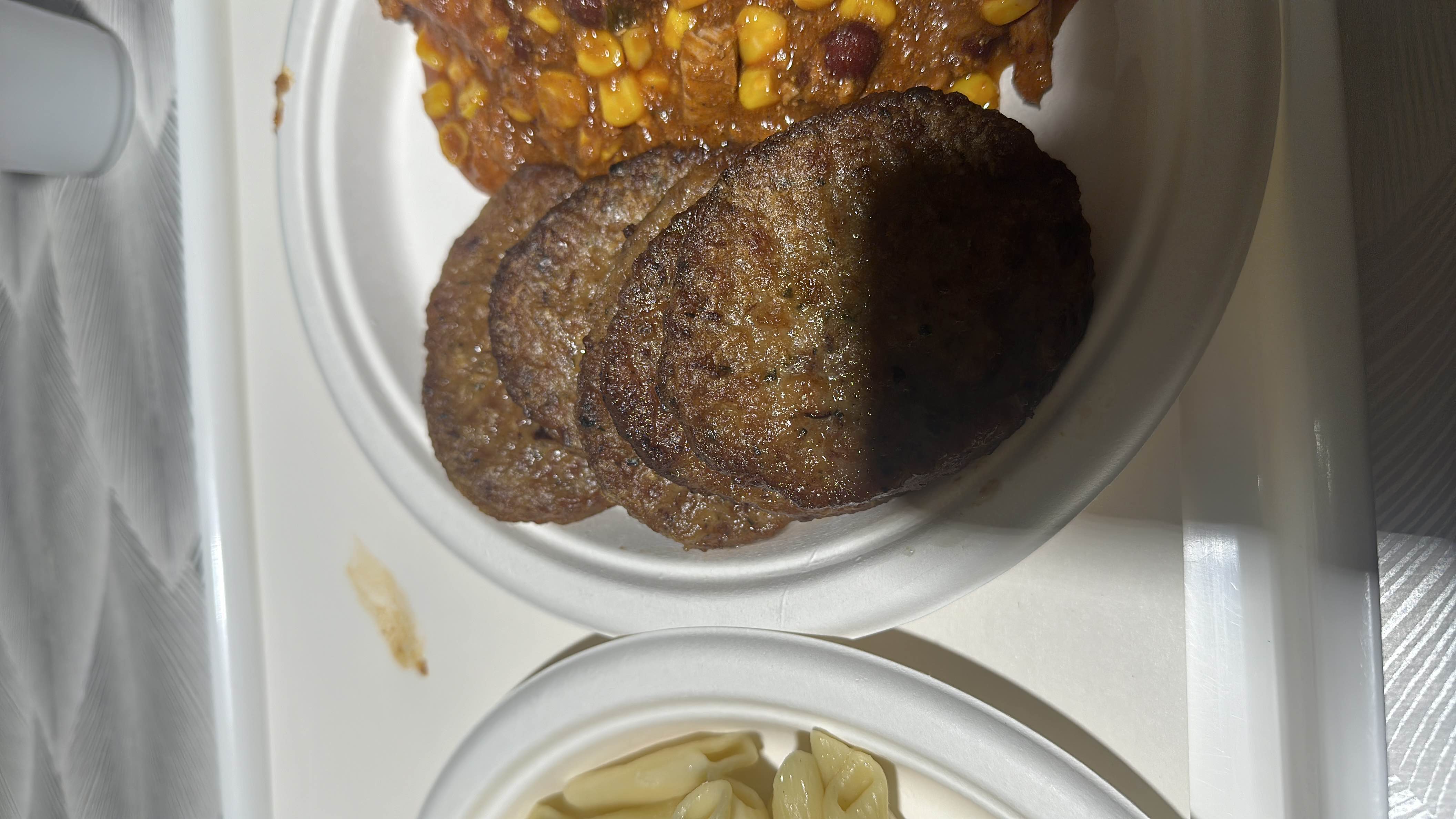 A meal consisting of beef patties, chili with corn and beans, and a side of pasta.