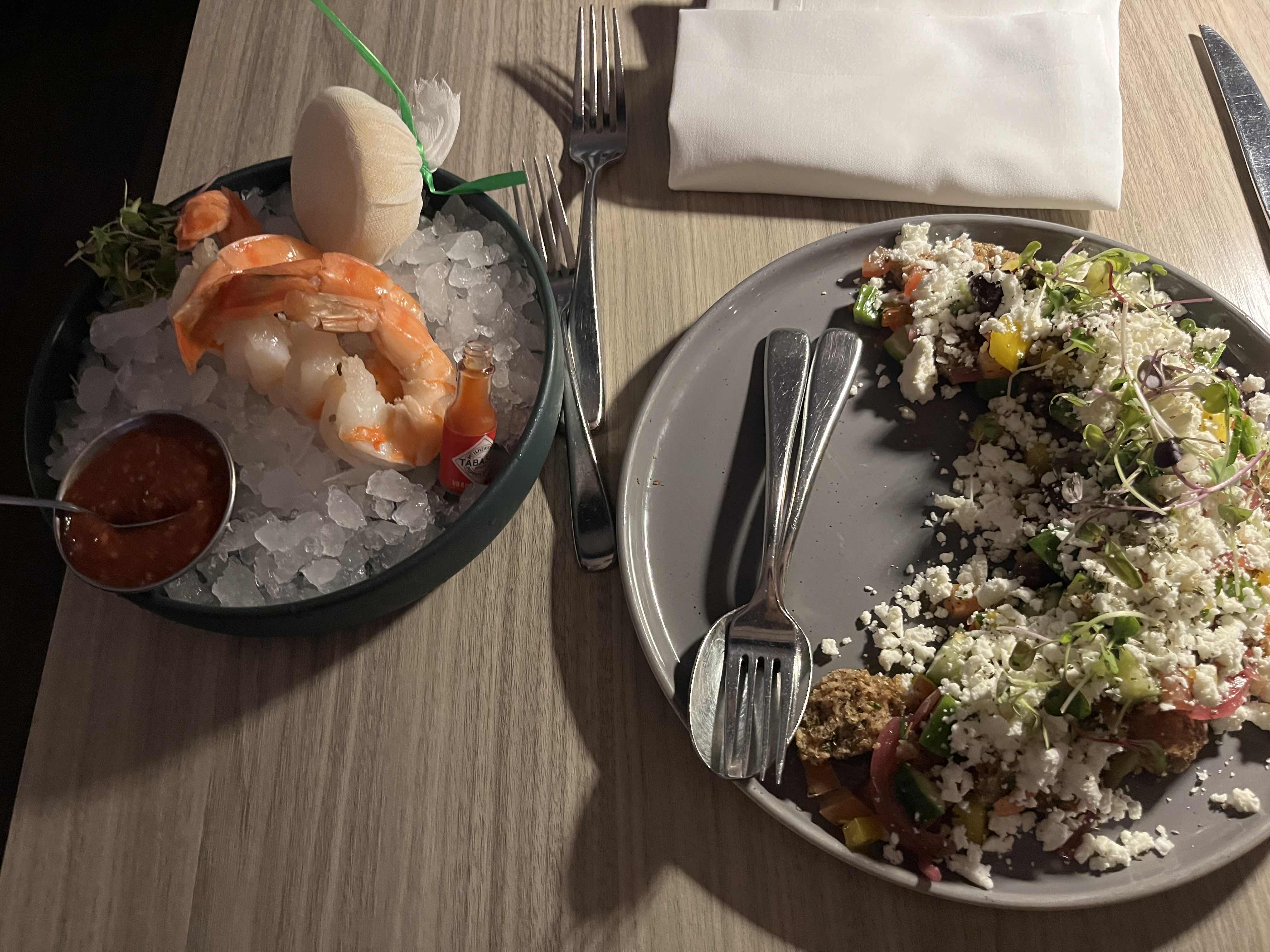 A dish featuring shrimp served on ice with salsa, accompanied by a salad of mixed vegetables, feta cheese, and microgreens.