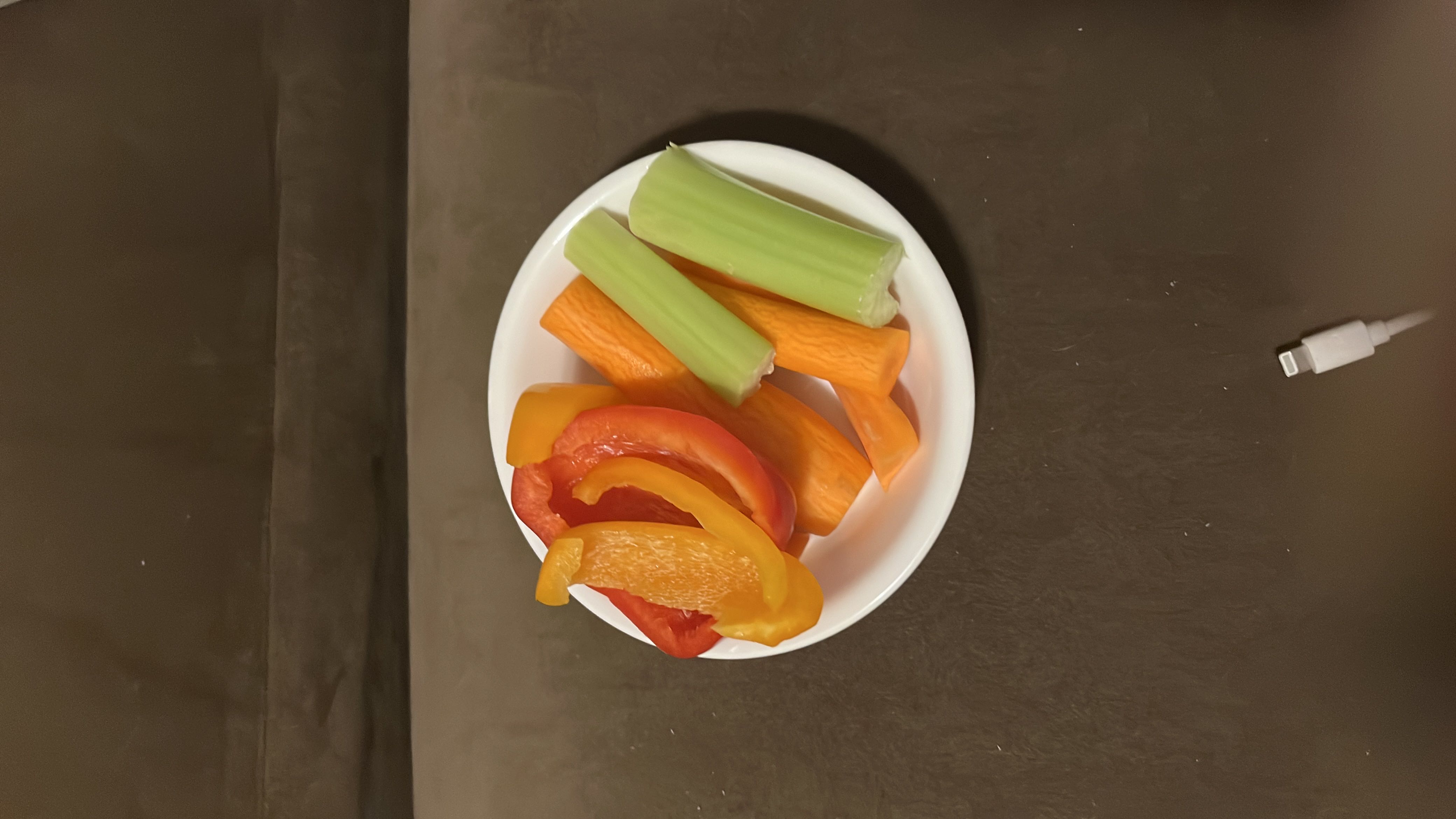 A plate of fresh vegetables including red and yellow bell peppers, carrot sticks, and celery sticks, providing a low-calorie, nutrient-rich snack.