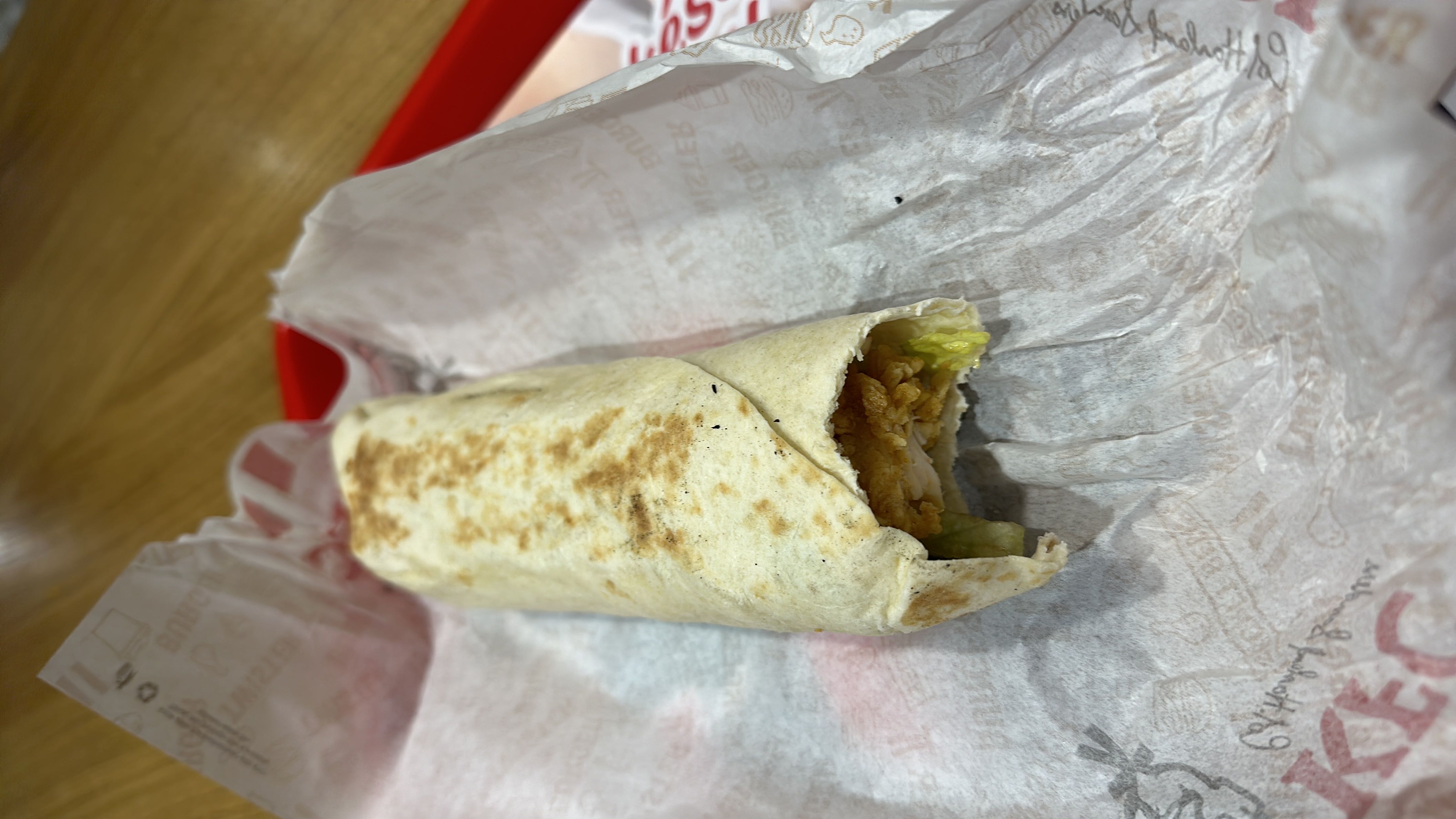 A wrap containing fried chicken, lettuce, and sauce, wrapped in a tortilla.