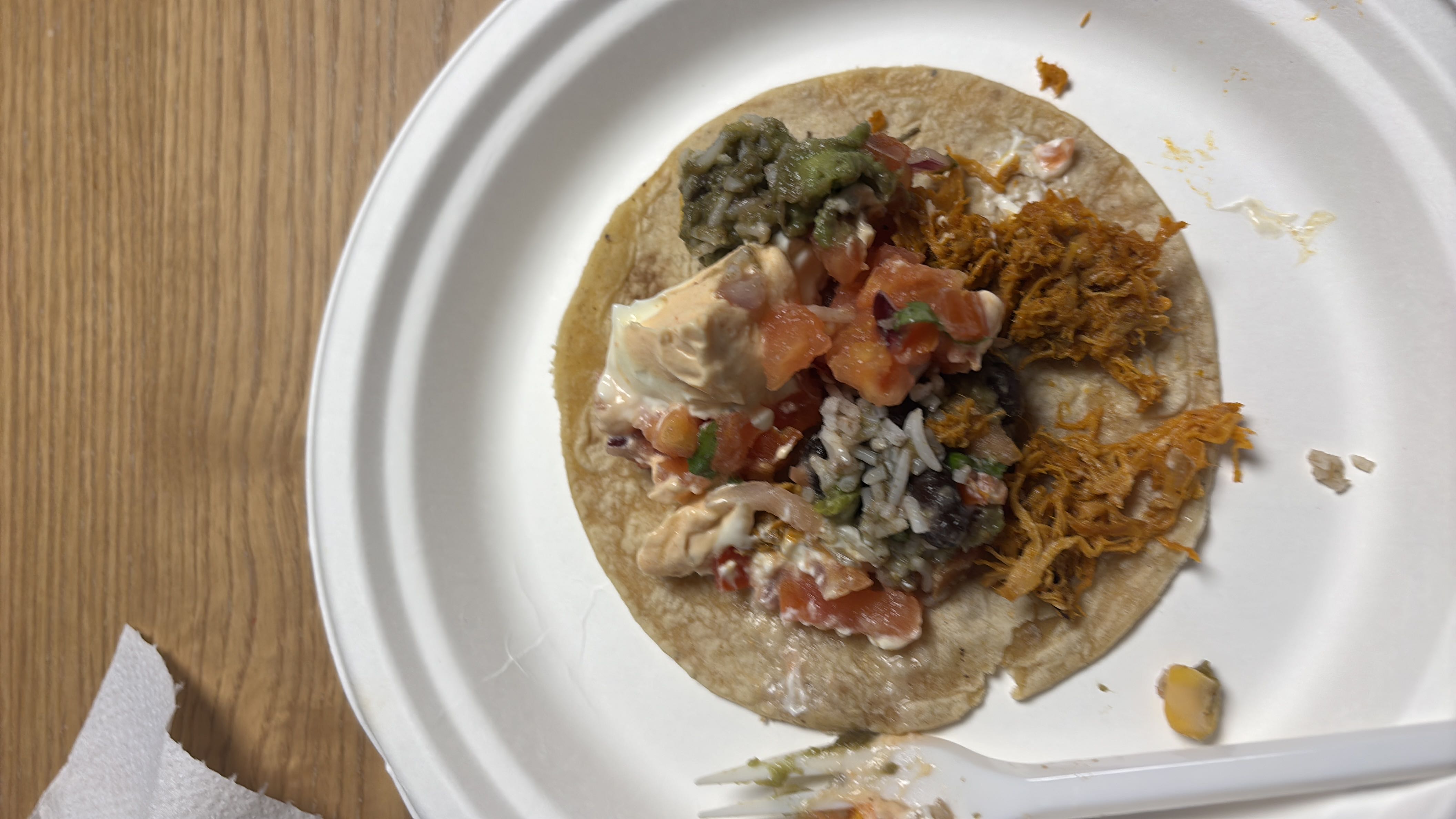 A taco with shredded chicken, guacamole, sour cream, pico de gallo, rice, and beans on a tortilla.