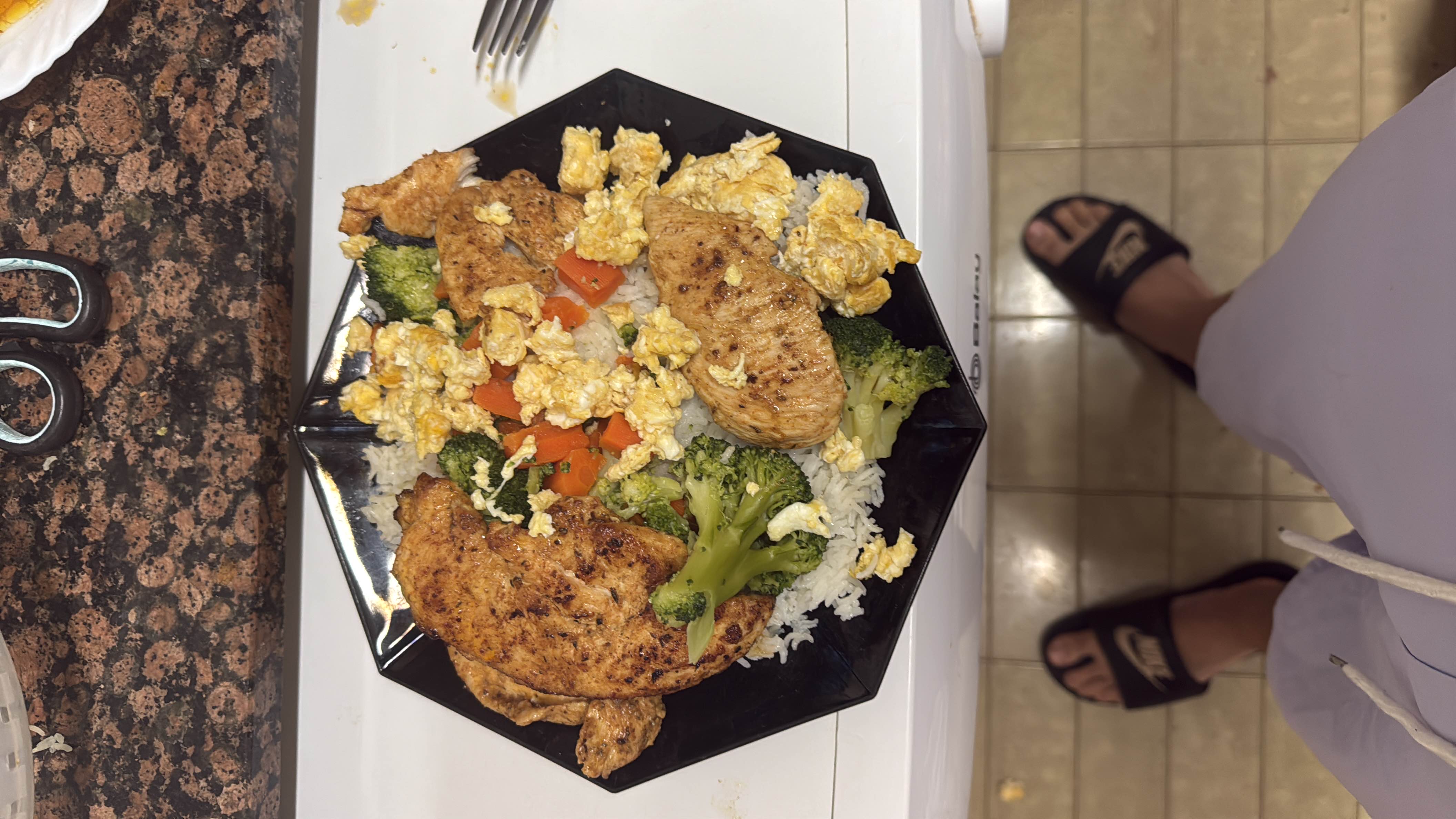 A balanced meal consisting of grilled chicken, rice, broccoli, carrots, and scrambled eggs, providing a good mix of protein, carbs, and fats.