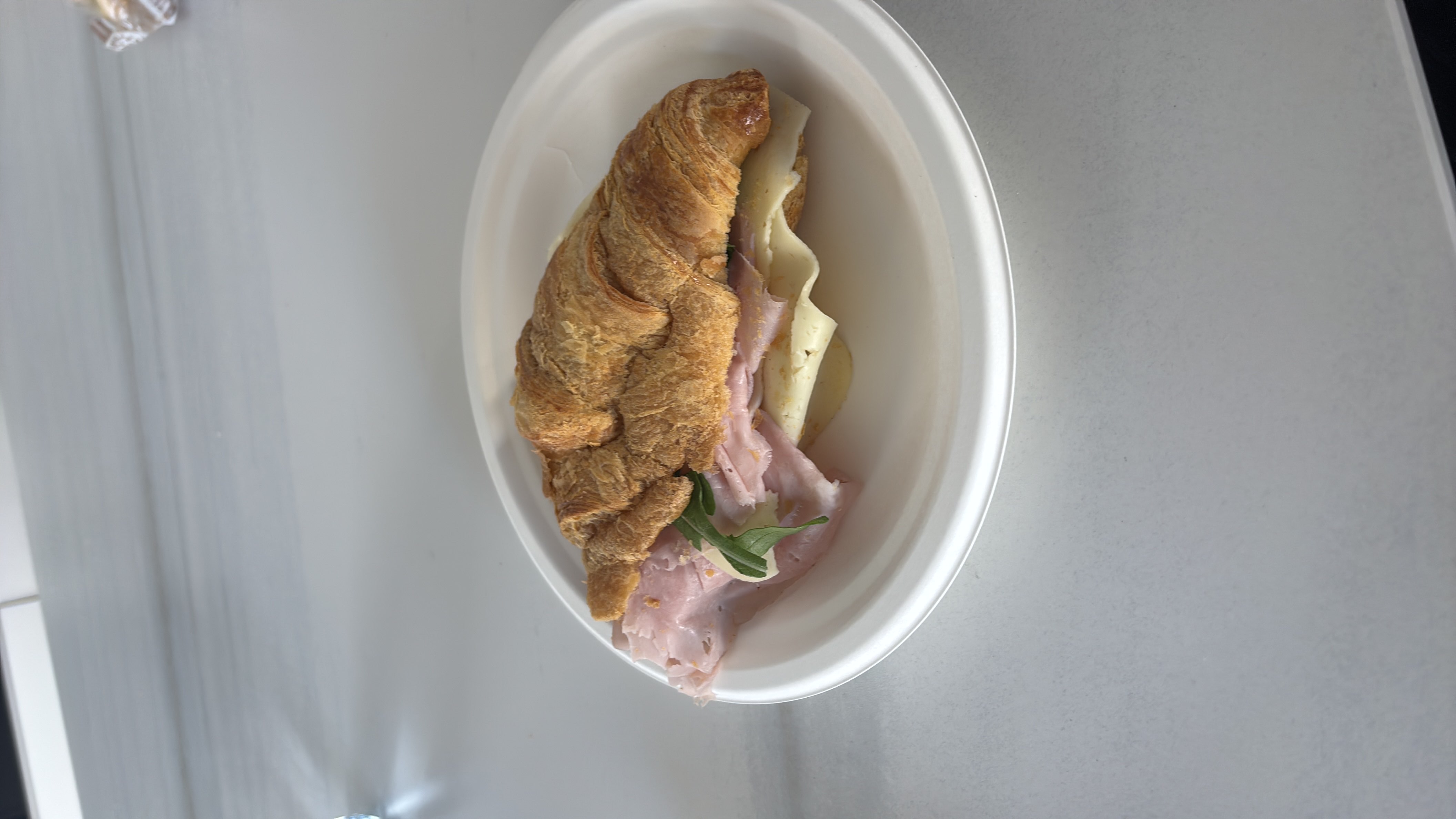 A croissant sandwich filled with ham, cheese, and a small amount of greens, providing a balanced mix of carbs, protein, and fats.