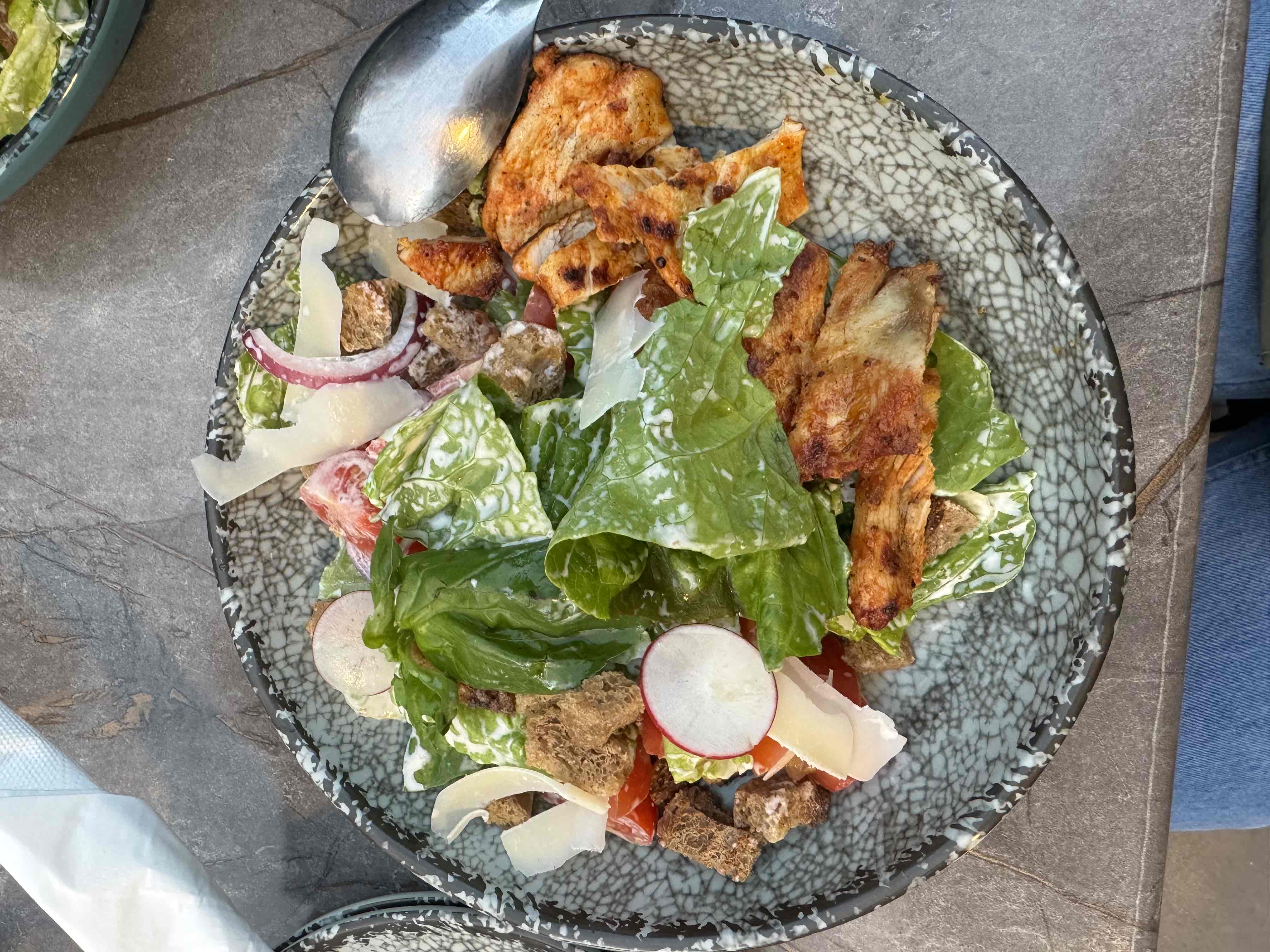 A Caesar salad with grilled chicken, lettuce, Parmesan cheese, croutons, radish, tomato, and Caesar dressing.