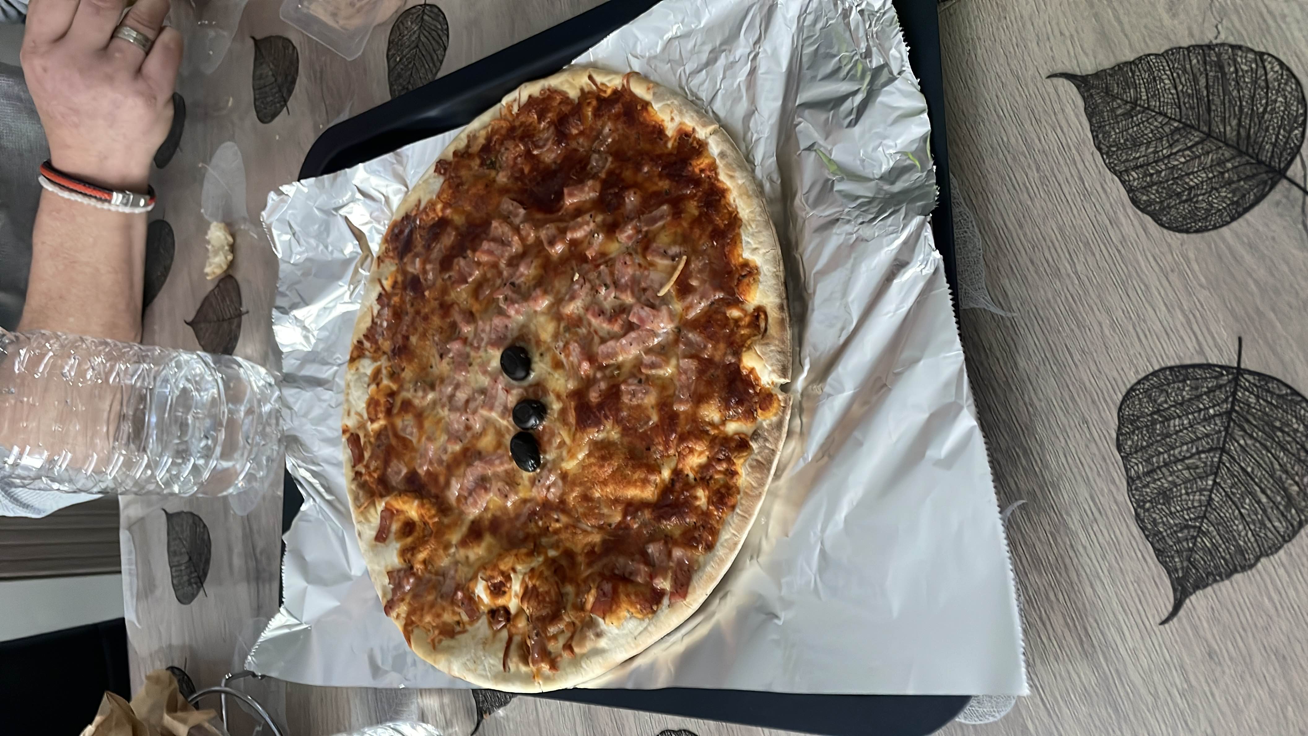 A baked pizza with cheese, ham, tomato sauce, and black olives on a thin crust.