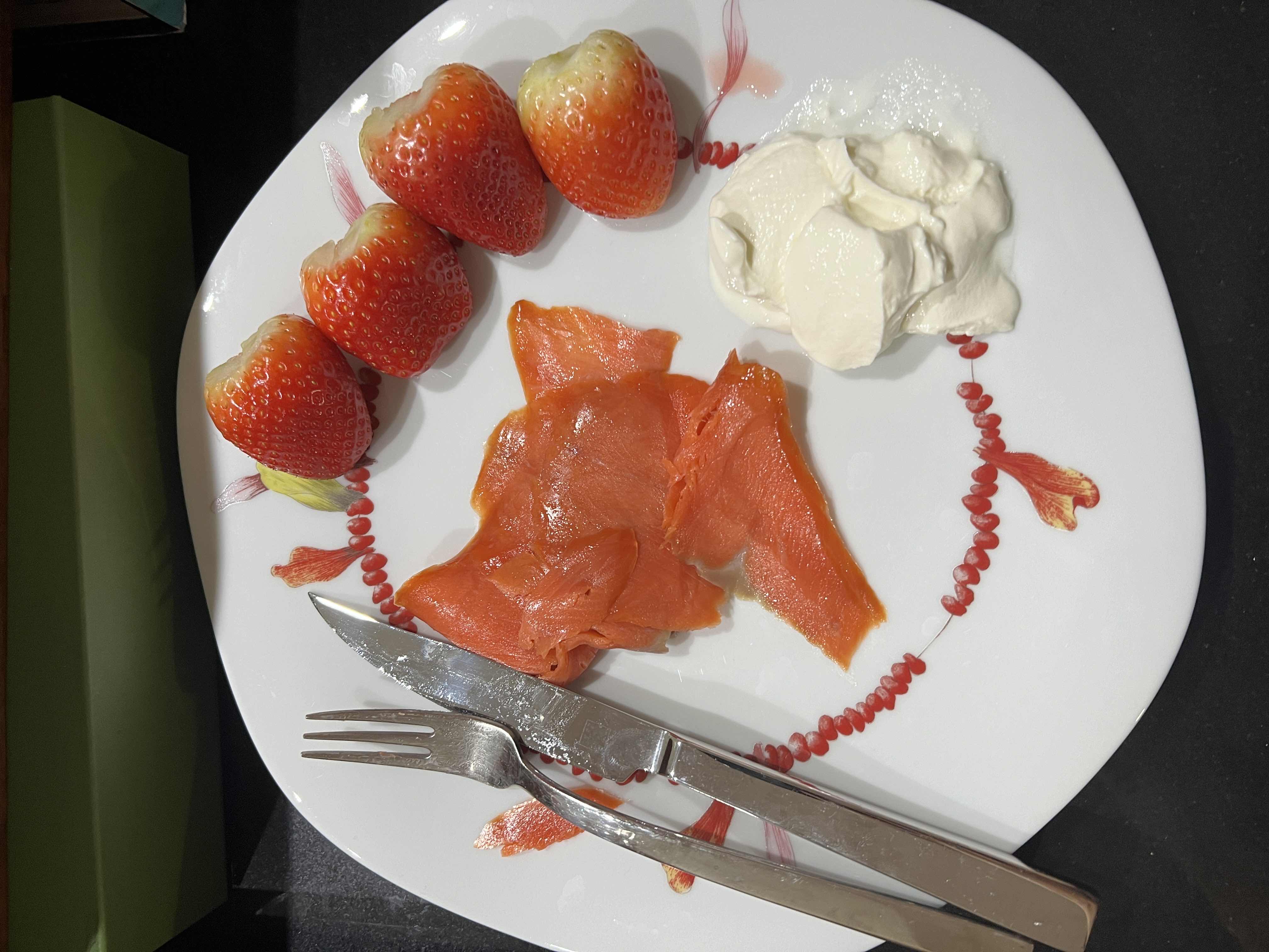 A plate containing smoked salmon, fresh strawberries, and a dollop of cream, offering a balanced mix of protein, carbs, and fats.