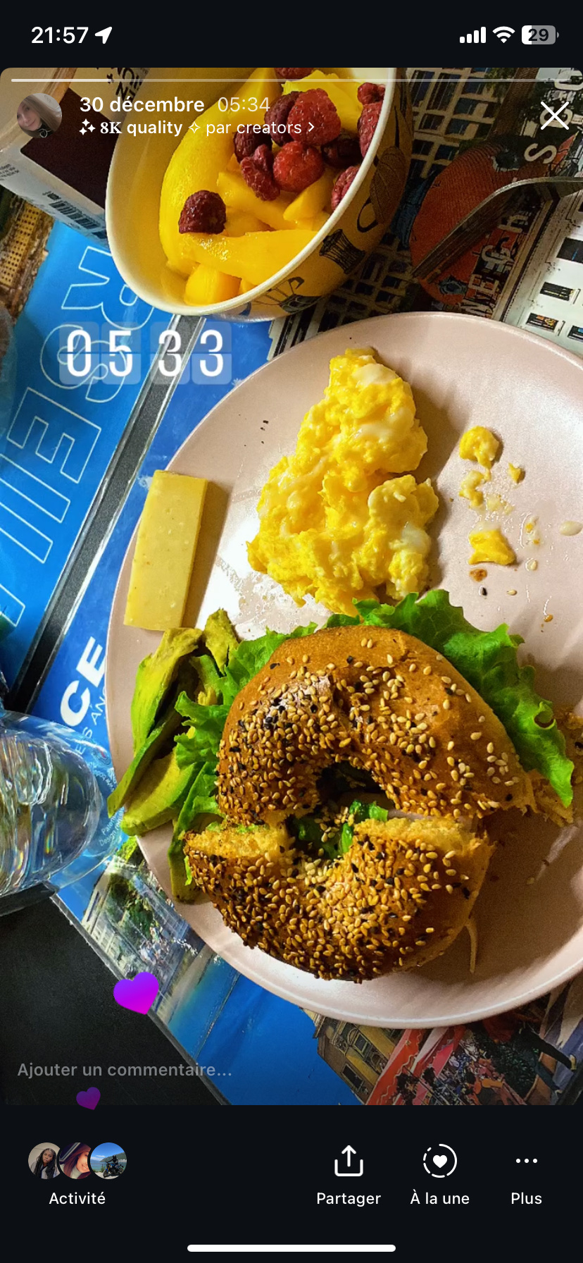 A balanced breakfast featuring a sesame bagel with lettuce, scrambled eggs, avocado slices, a cheese slice, and a fruit bowl with mango and raspberries.