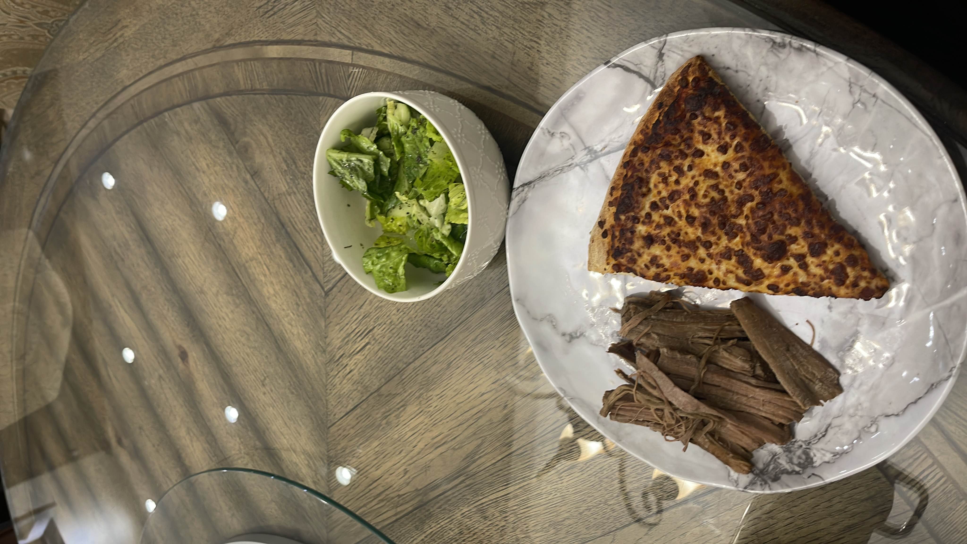 Roast beef with a slice of pizza and a salad that is made of cucumbers and lettuce.